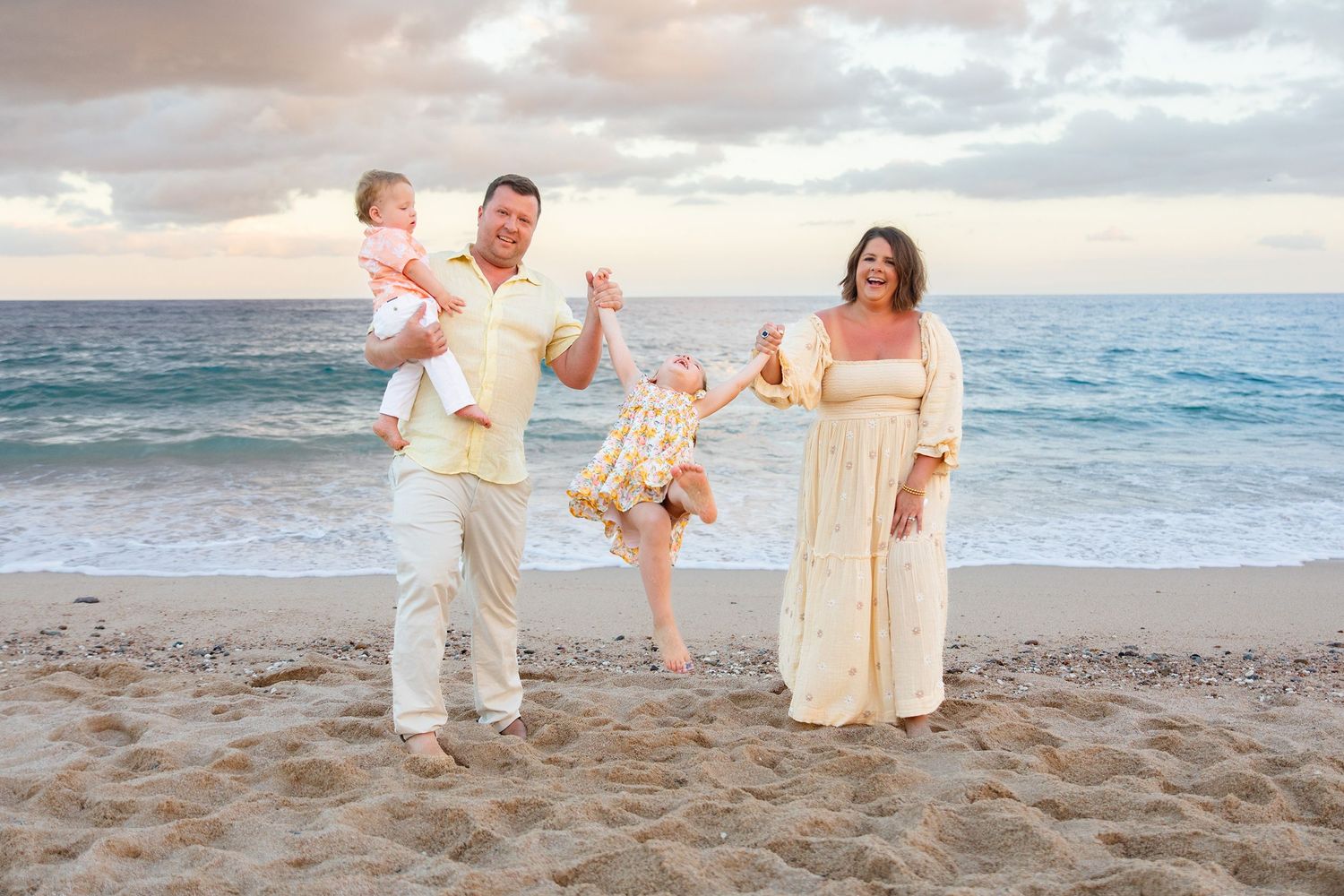 Playful family of four on beach at sunset, parents swinging children with joy.