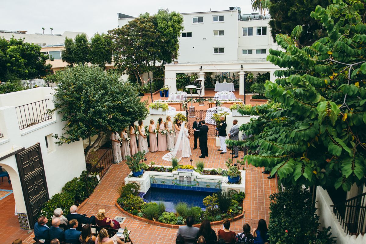 Aerial view of outdoor wedding ceremony in Spanish courtyard with fountain and wedding party.