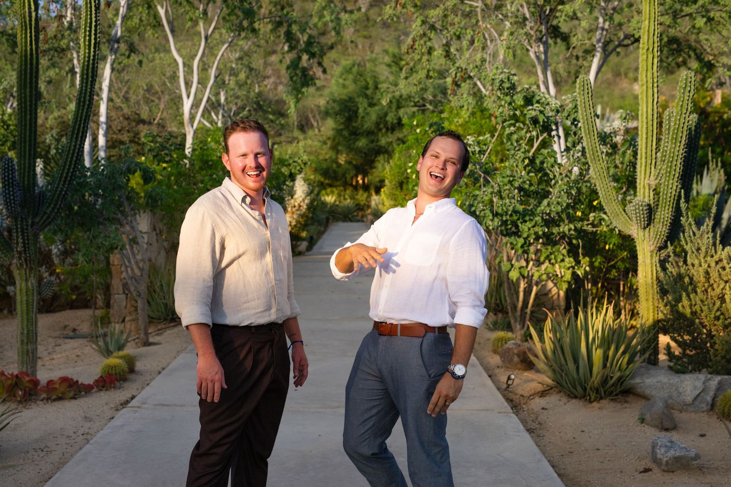 Two men smiling on a desert garden path surrounded by cacti and lush greenery in warm sunlight acre resort