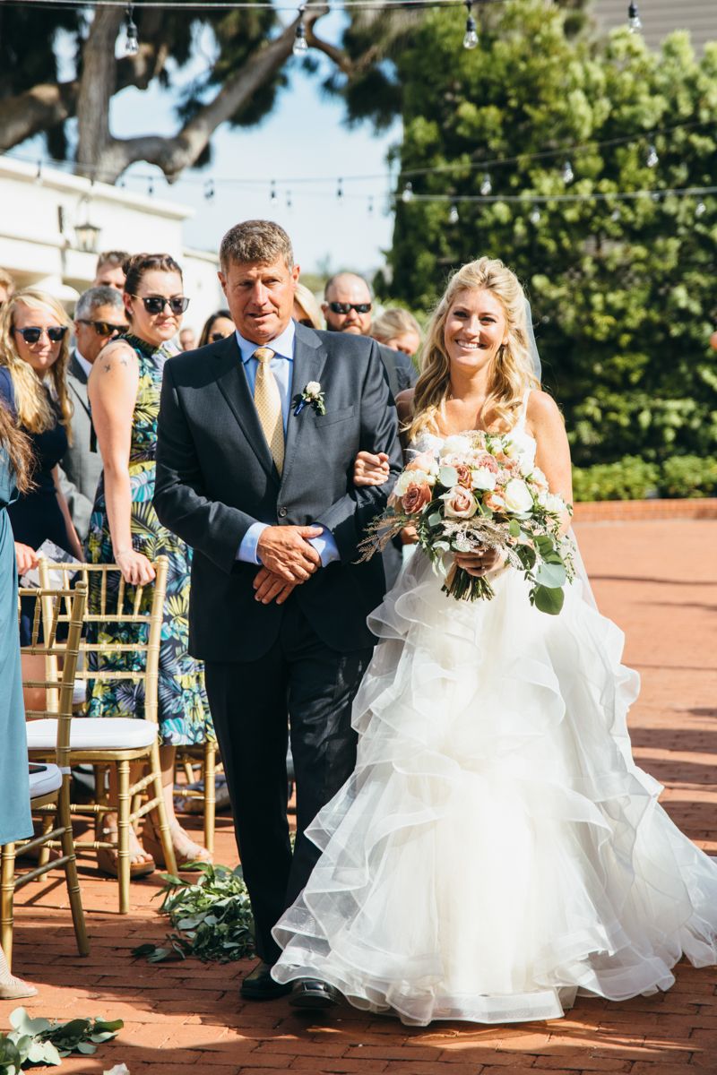 Smiling bride walking down the aisle with her father at an outdoor wedding ceremony.
