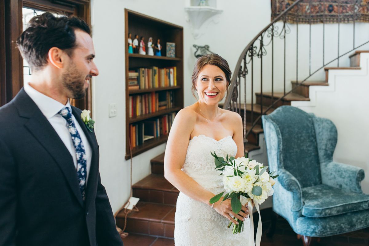 Bride and groom sharing first look moment in elegant library staircase, bride holding white bouquet.