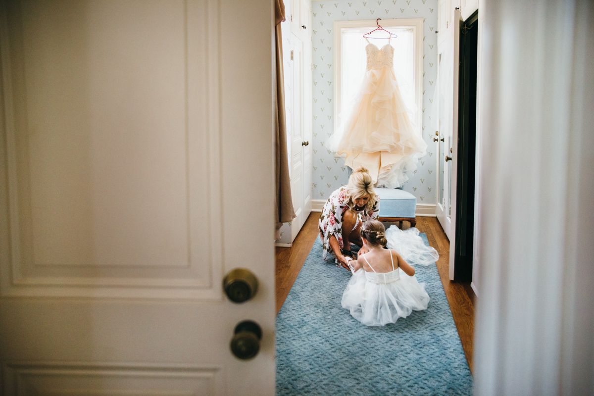 Bride getting dressed in elegant room with wedding gown hanging in background.