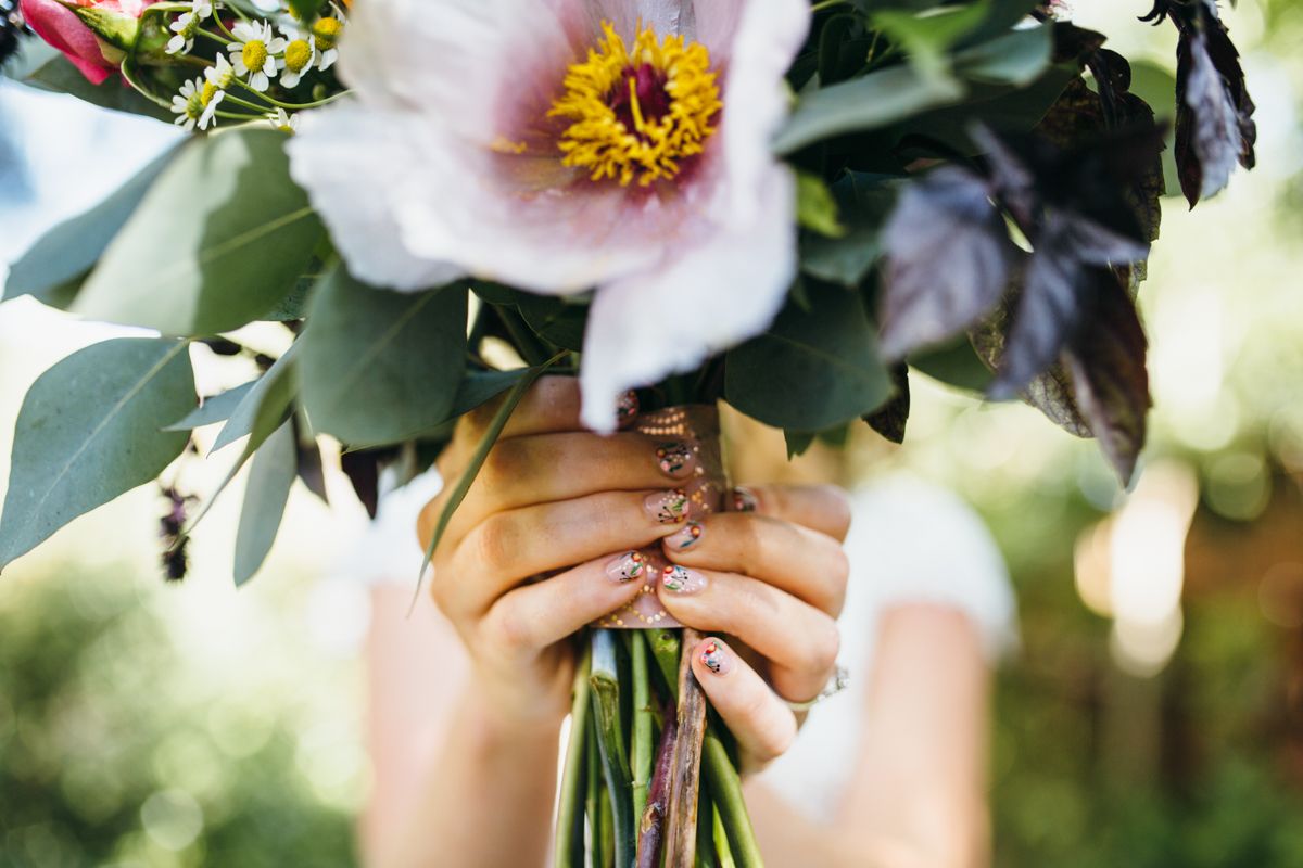 Close-up of bride holding lush bouquet with white peony and dark foliage, showing glitter nail art.