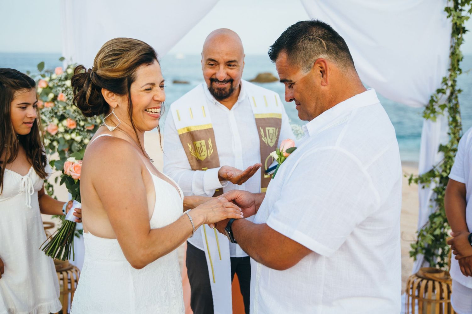 Couple exchanging rings at a romantic beach  in Cabo San Lucas wedding ceremony with floral decorations and an officiant.