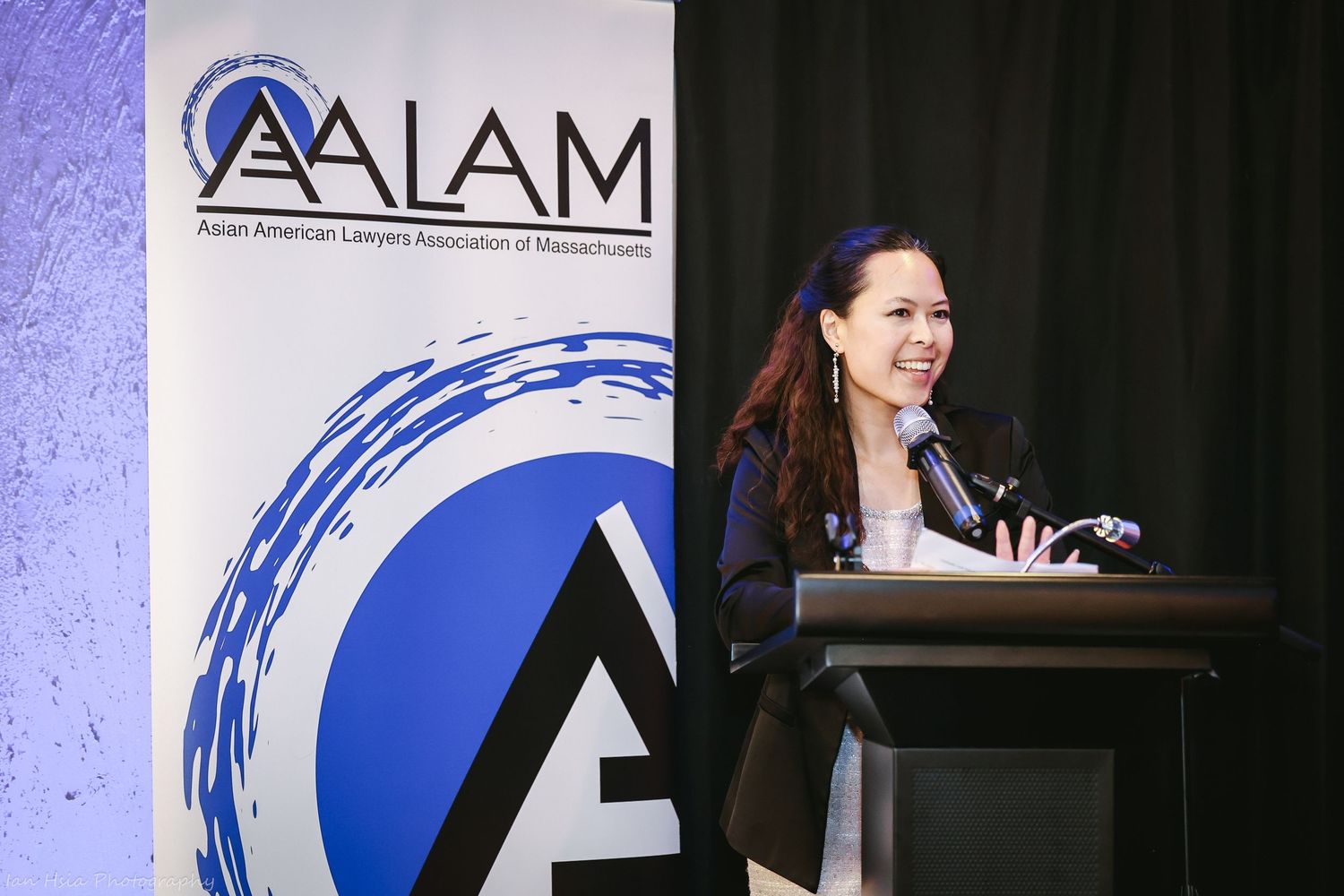 Speaker presenting at AALAM conference podium with organization banner displayed.
