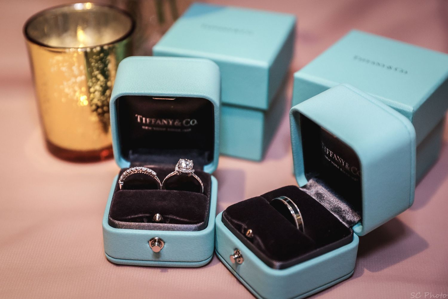 Engagement rings displayed in light blue Tiffany-style jewelry boxes on pink surface.