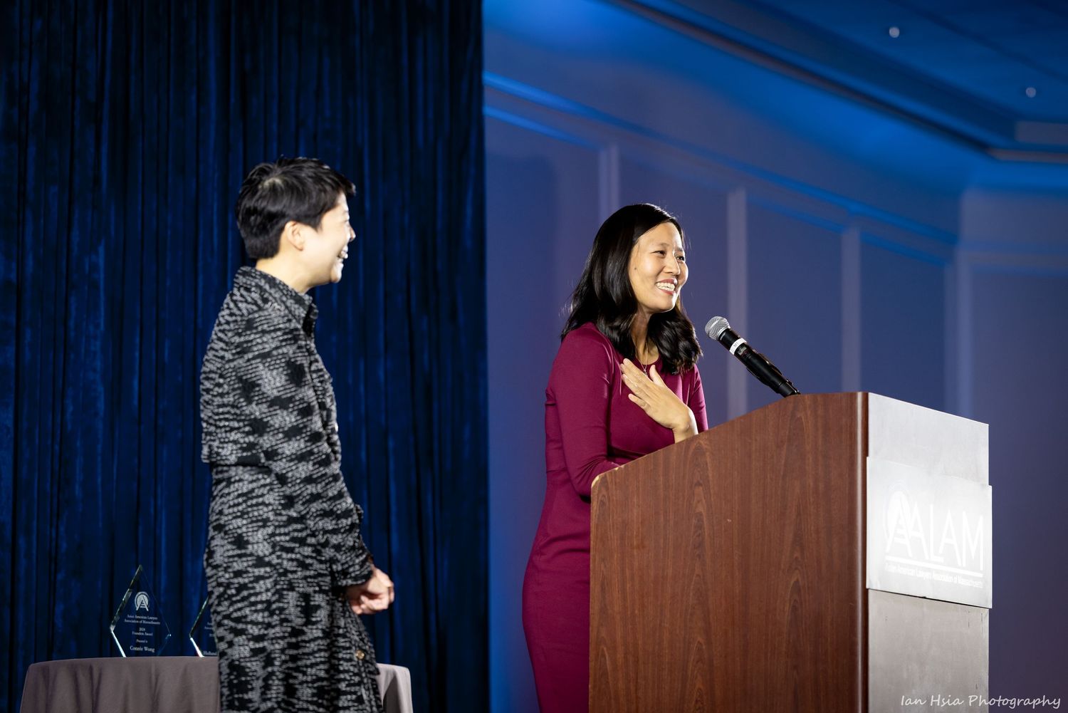 Speakers presenting at a professional conference with blue curtain backdrop and podium.