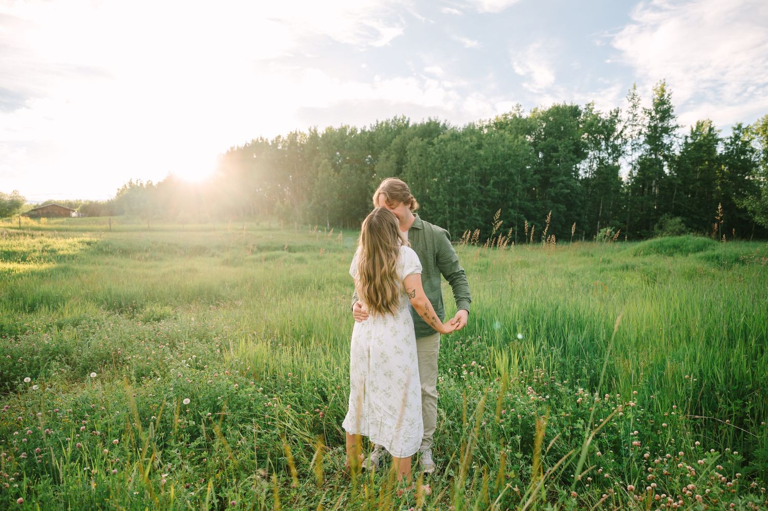 Couple dancing in a sunlit green meadow with trees in the background during golden hour.