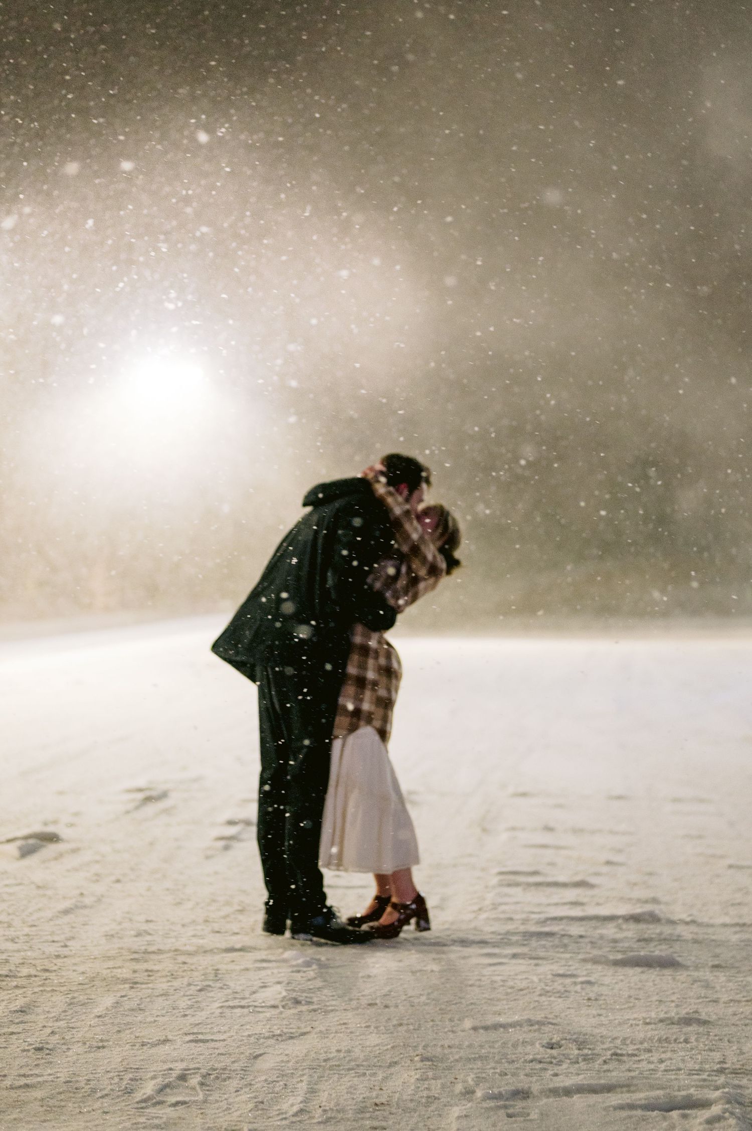 A romantic couple embraces in a snowy winter landscape during a gentle snowfall.