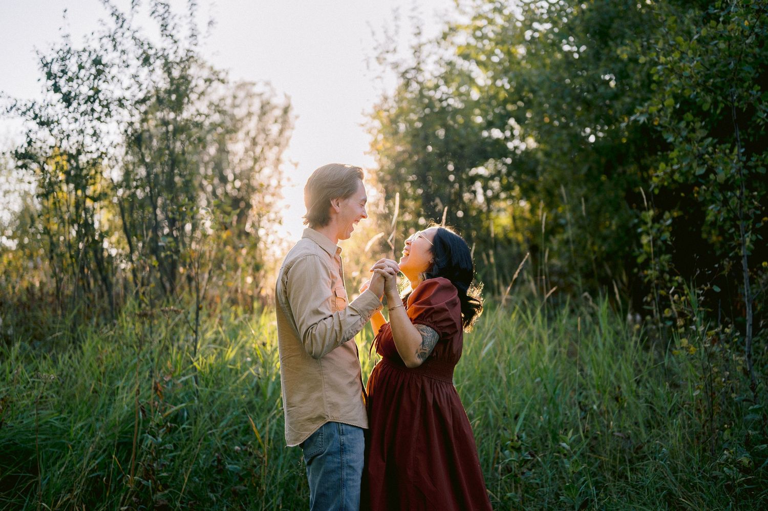 A couple enjoys a romantic moment in tall grass during golden hour sunset.