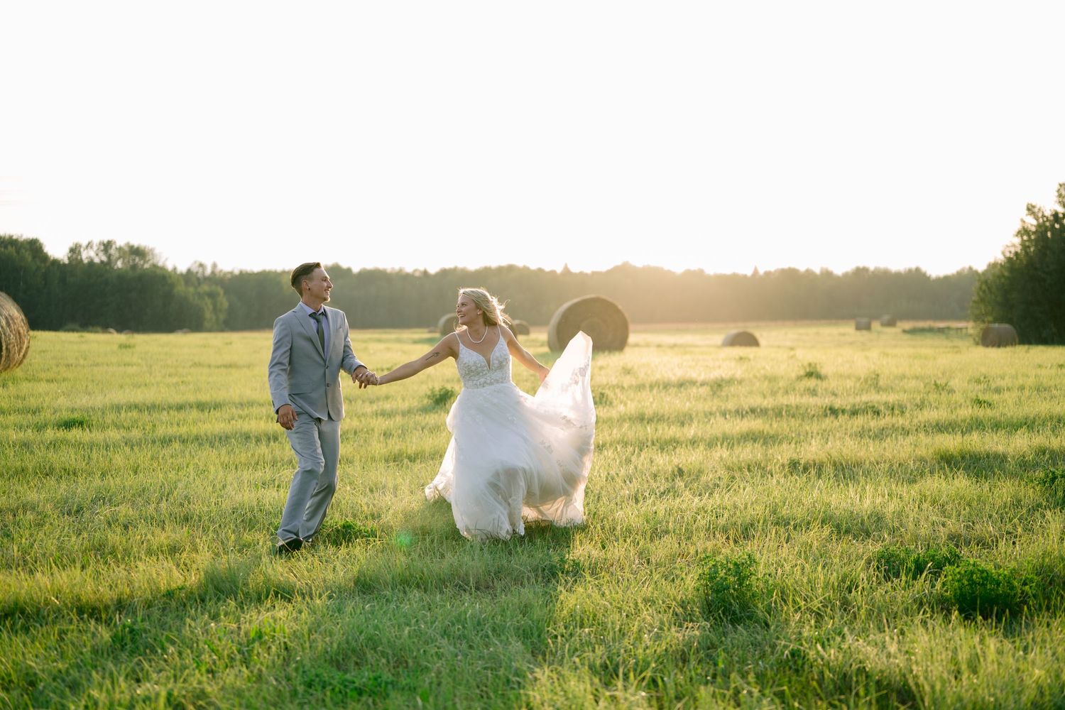 A couple dances together in a sunlit meadow during golden hour, with the bride's white dress flowing in the breeze.