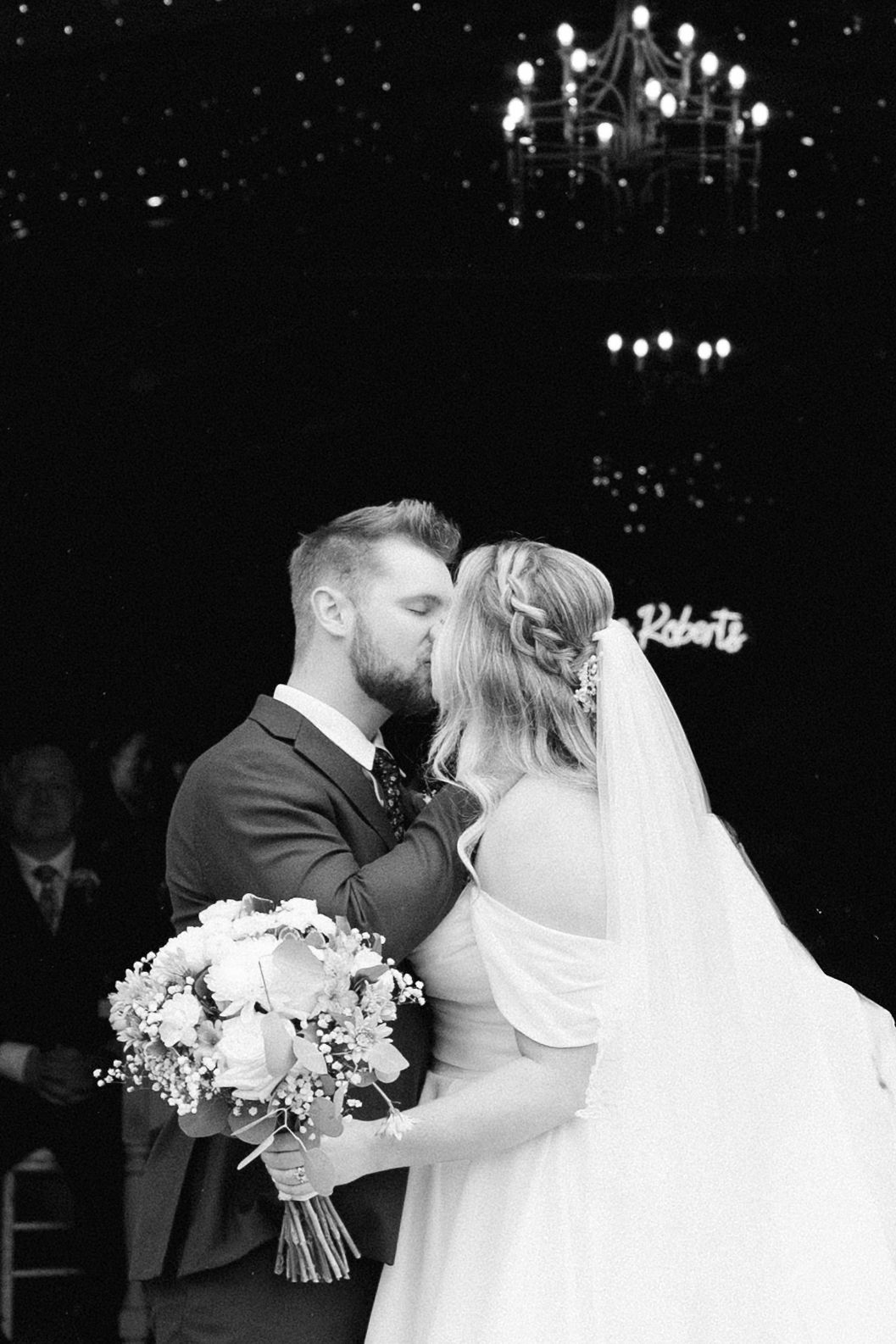Black and white wedding portrait with chandelier lighting and bridal bouquet.