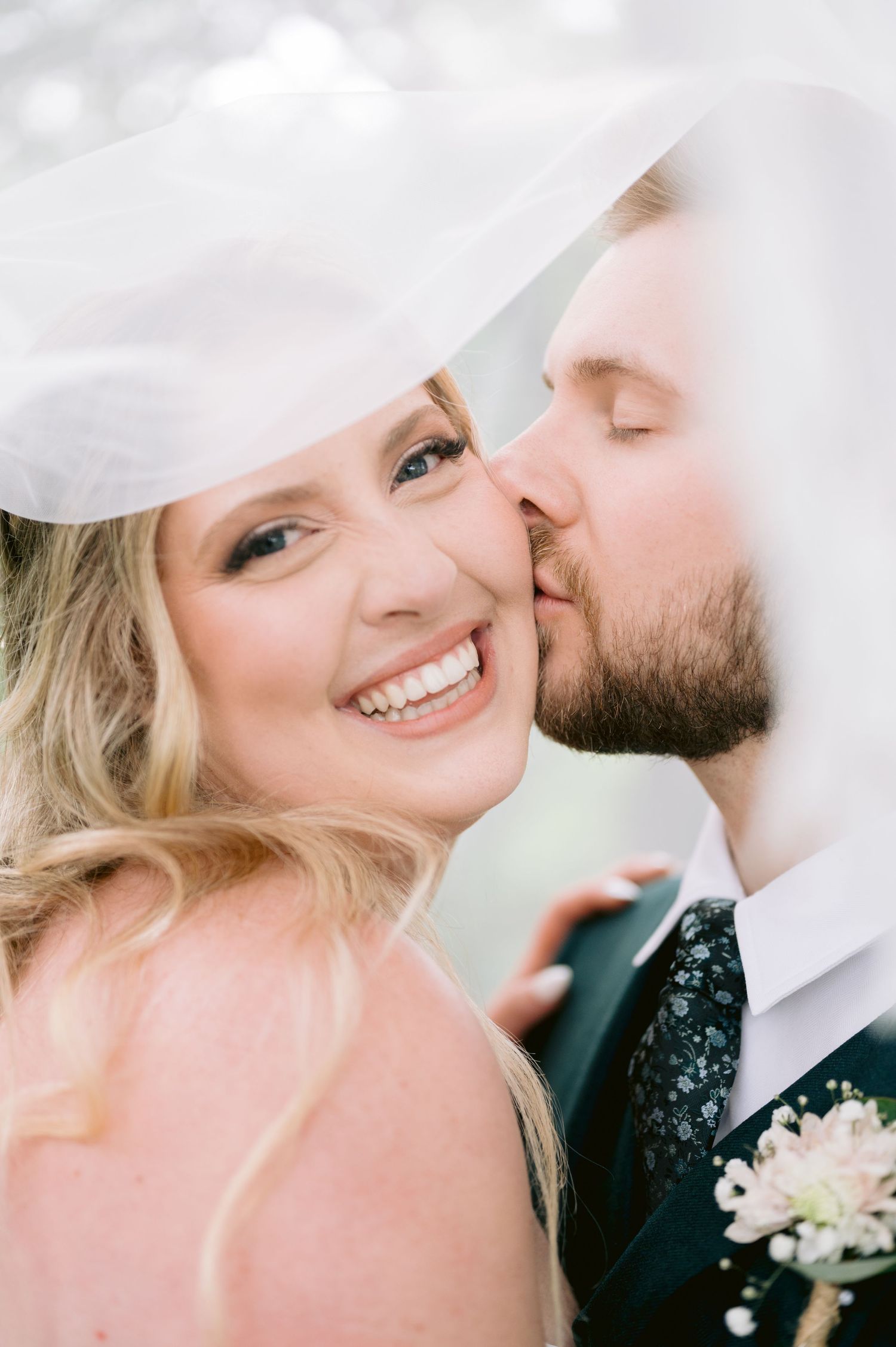 Intimate wedding portrait with bride smiling under veil.