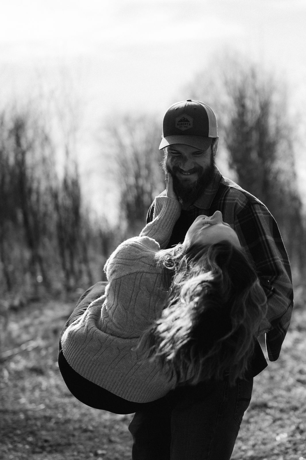 A couple embracing in a tender moment outdoors on a hillside in black and white photography.