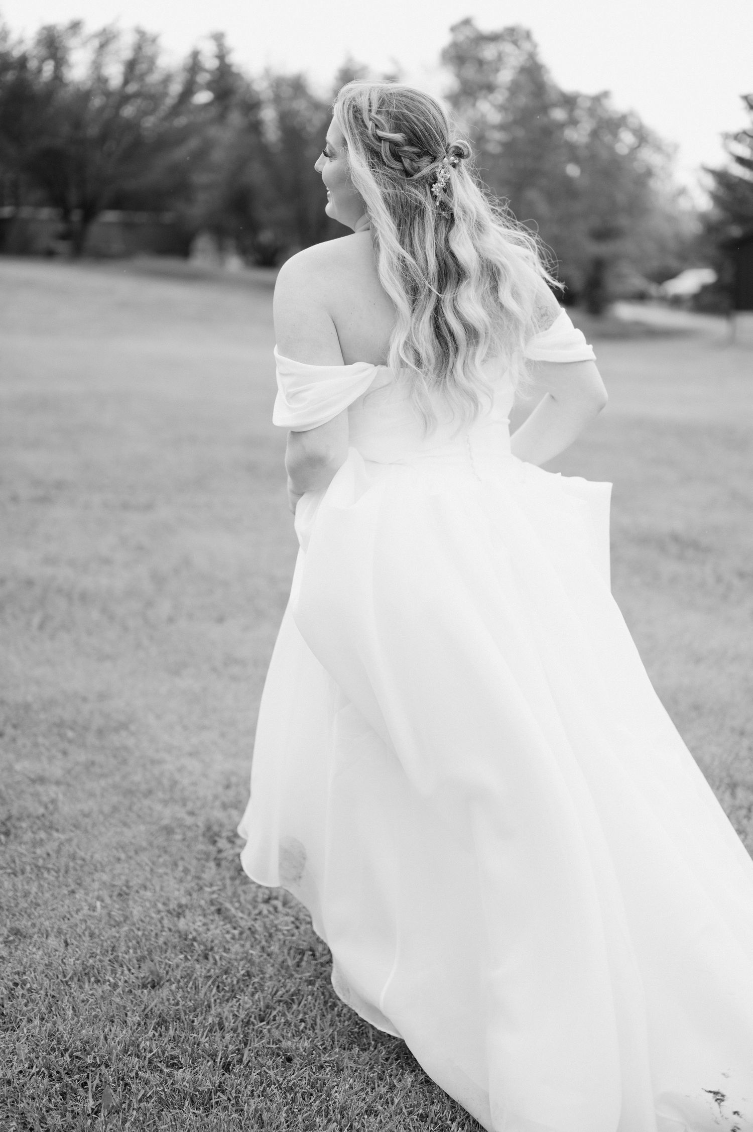 Bride in off-shoulder wedding dress posing in outdoor black and white portrait.