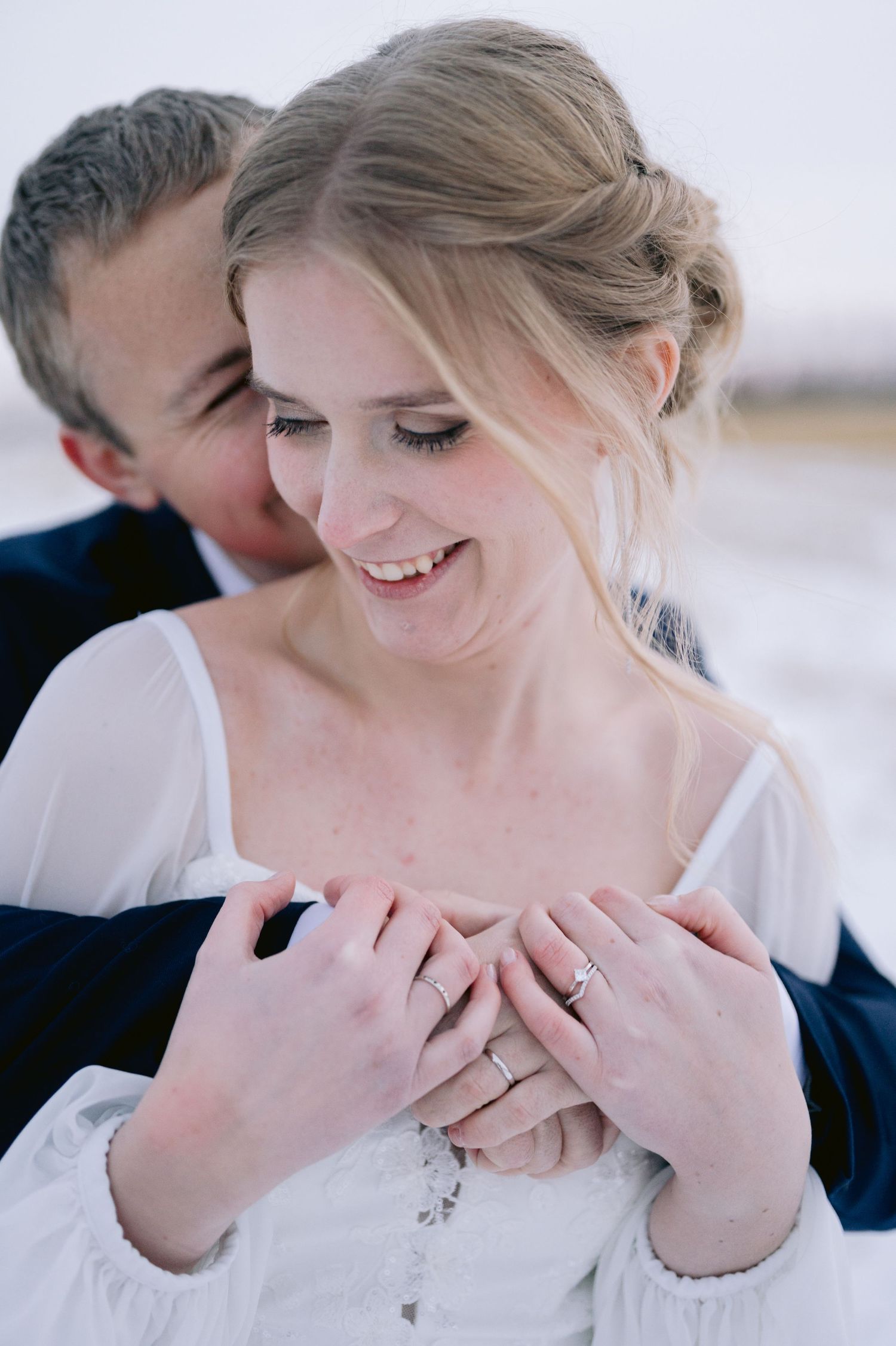 A couple shares intimate moments together in a snowy winter setting wearing white and navy formal attire.