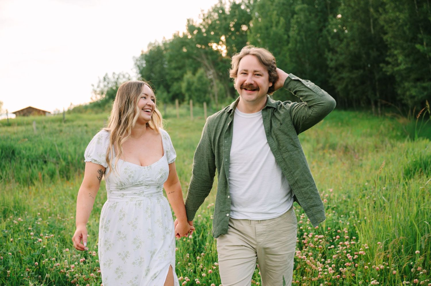 A happy couple walks hand-in-hand through a lush green meadow, smiling and laughing on a sunny day.