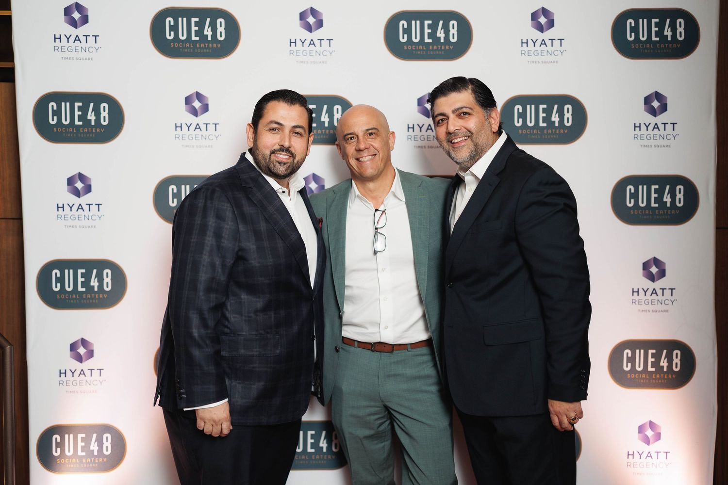 Three people in formal attire pose together against a branded backdrop with Hyatt and Chefs logos.