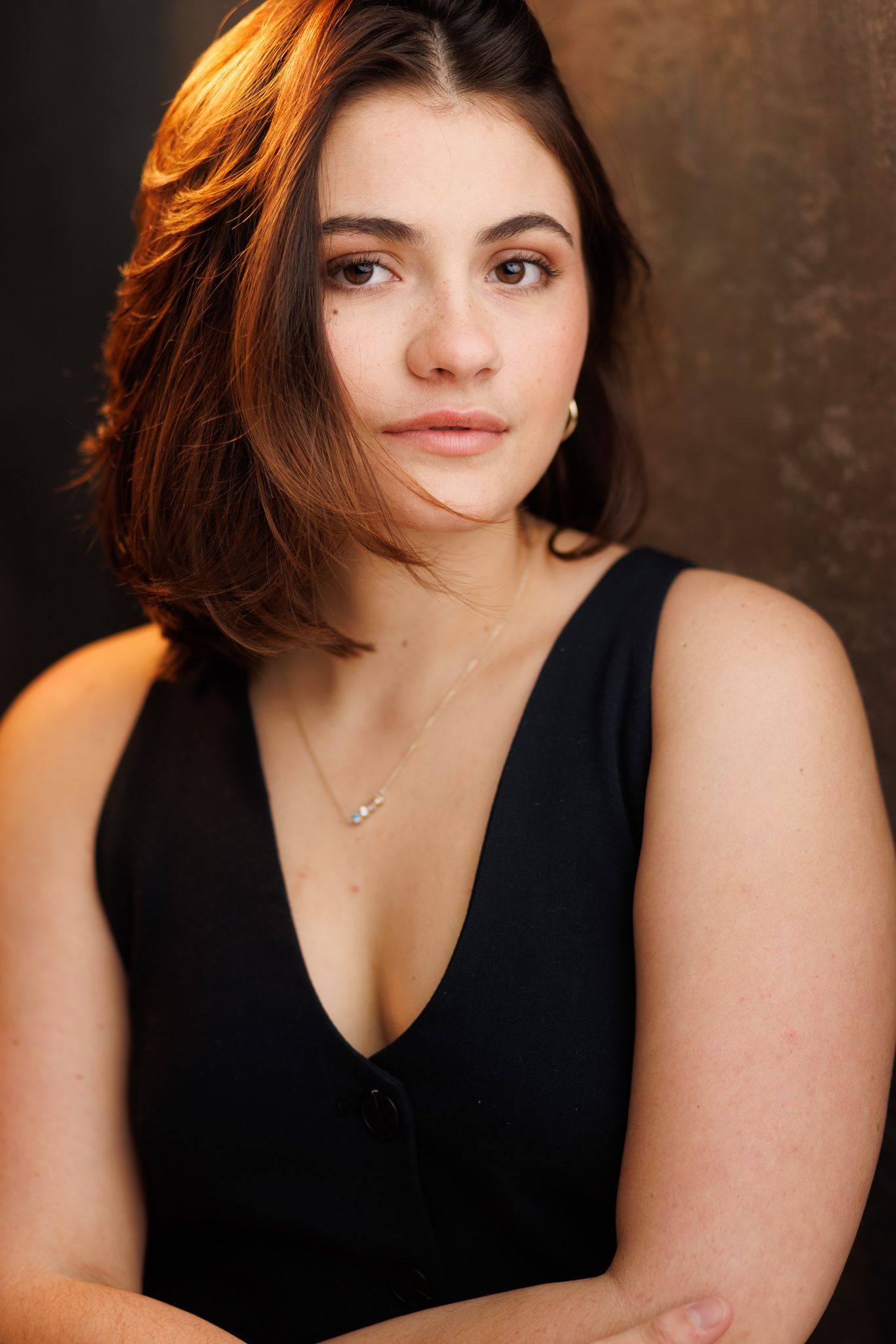 Studio portraits in black sleeveless top against warm-toned background.