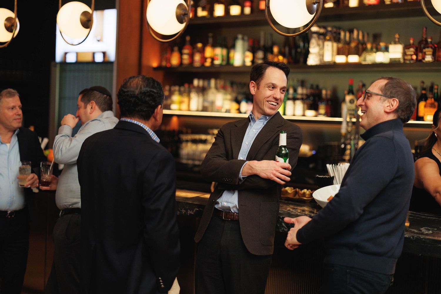 People socializing and enjoying drinks at an elegant bar with warm ambient lighting and Japanese paper lanterns.