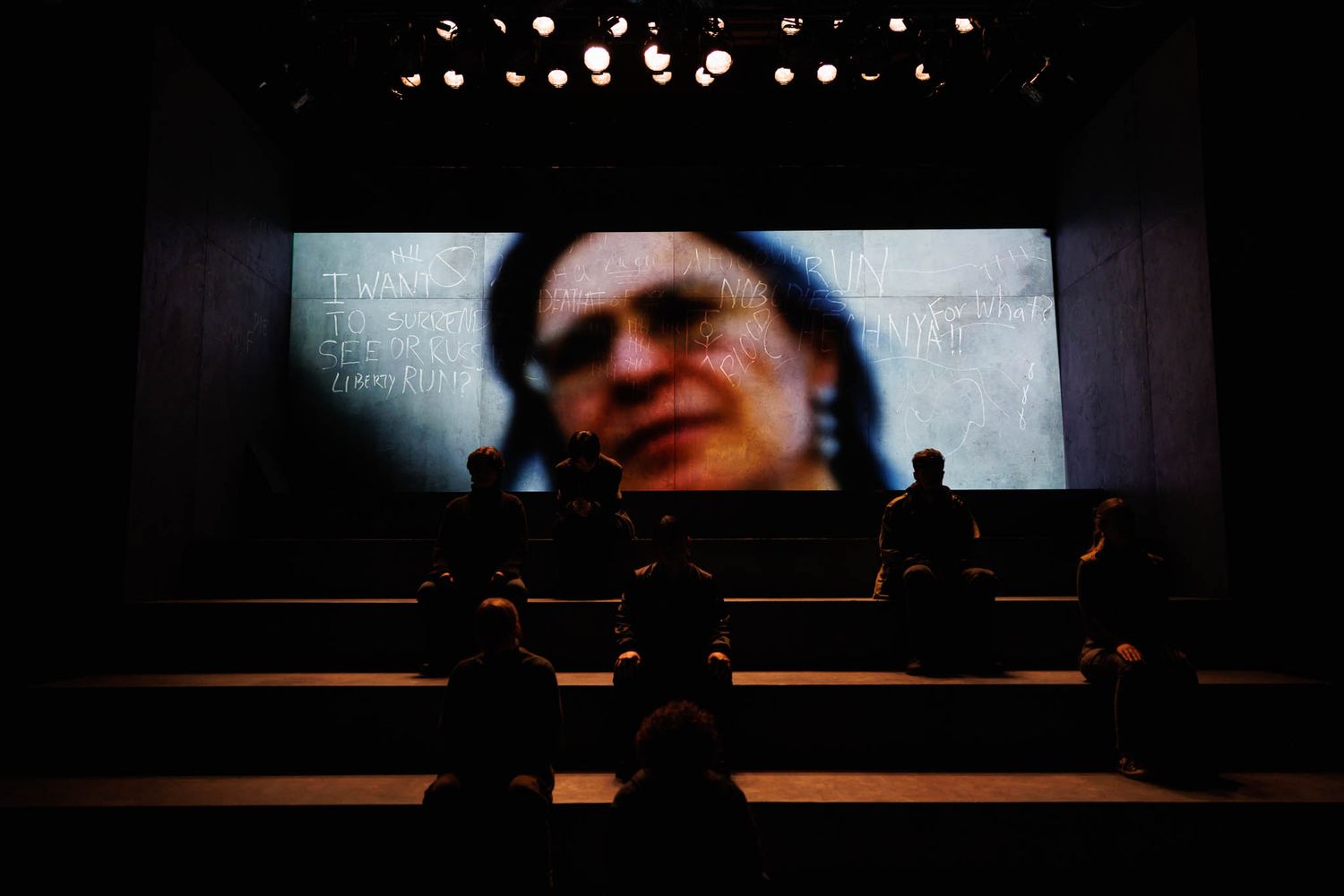 Silhouettes of people watching a large projected video screen in a dark theater.