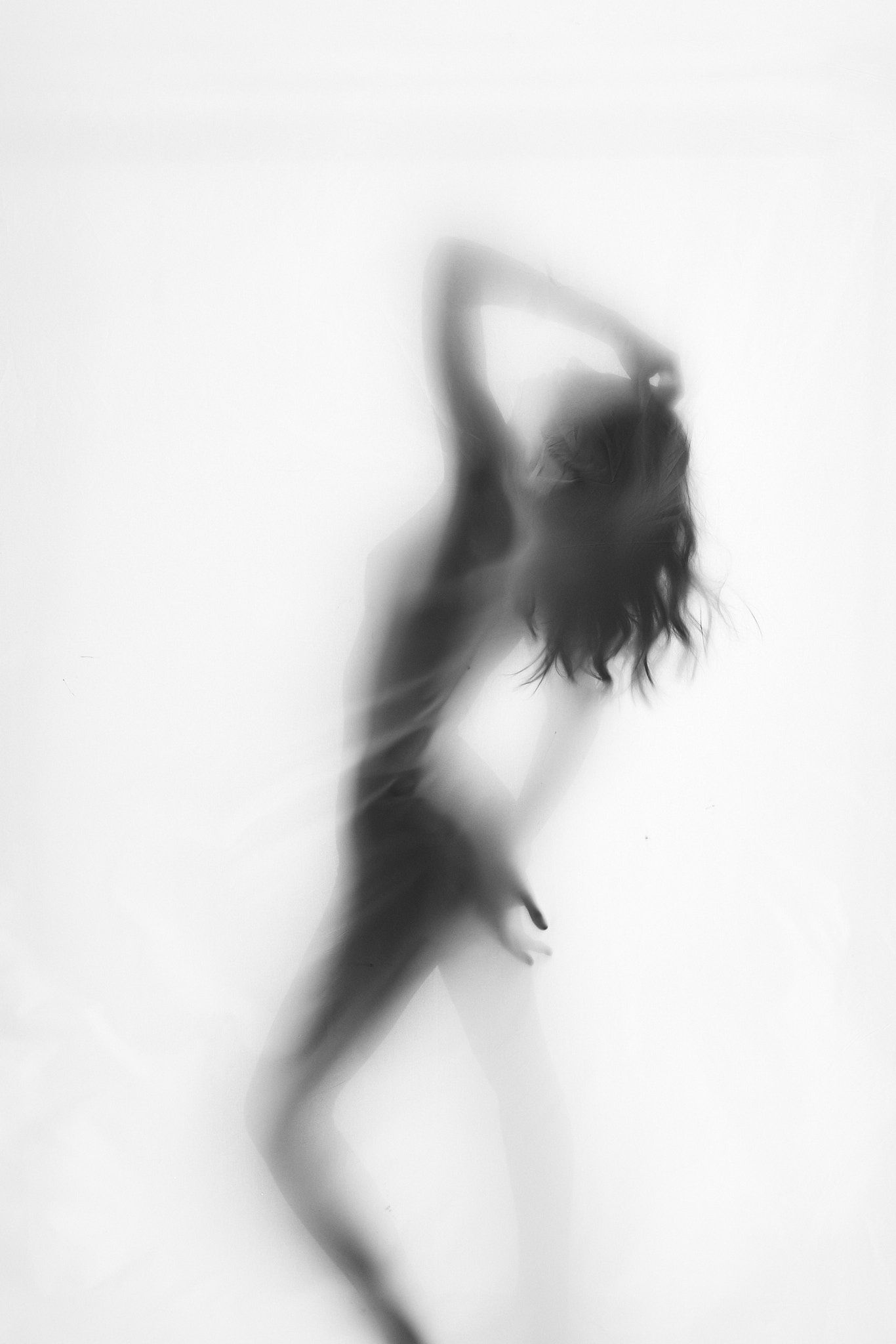 Blurred black and white silhouette of a woman dancing gracefully behind a translucent white surface.