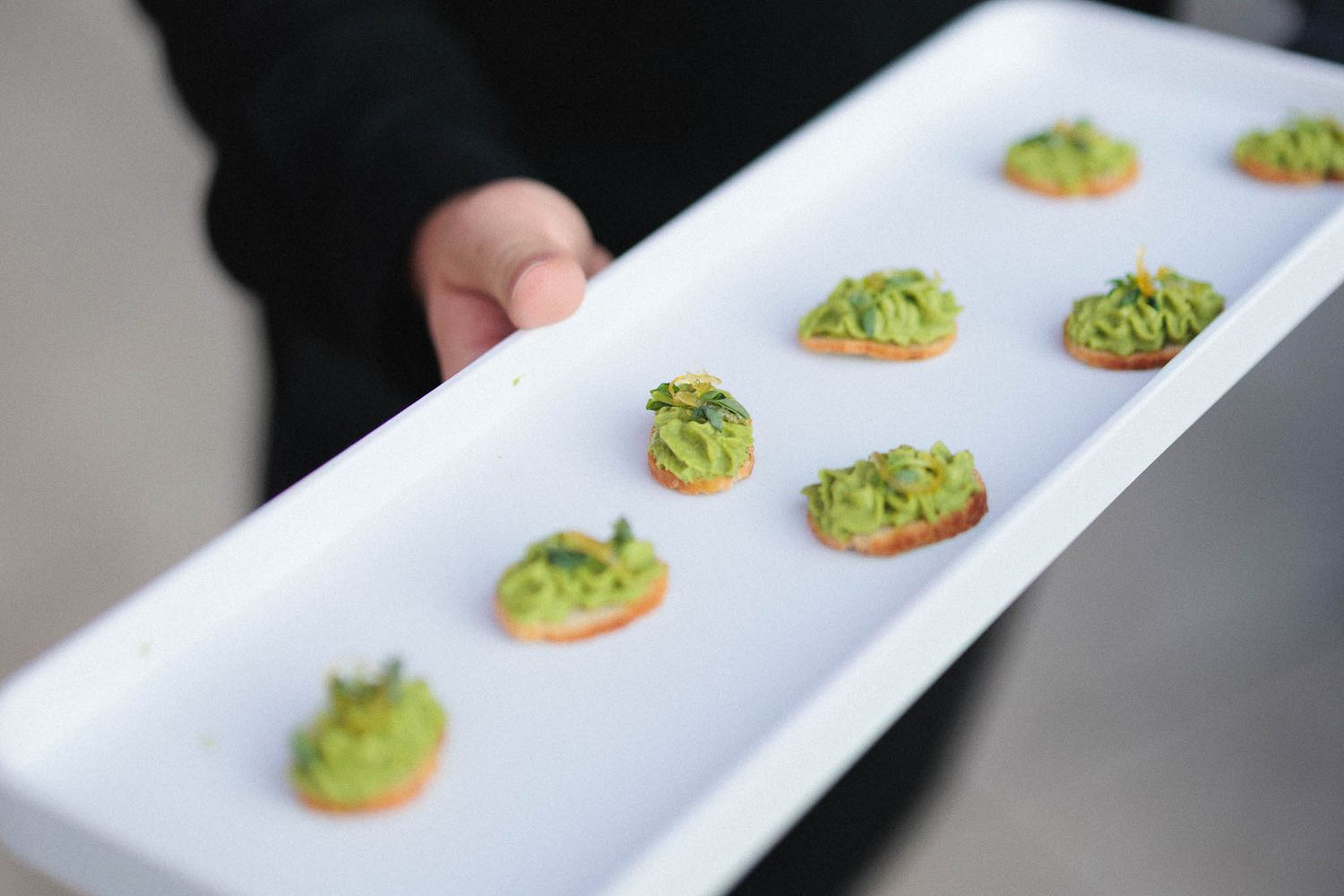 Green avocado spread being piped onto small round crackers arranged in a row on a white serving platter.