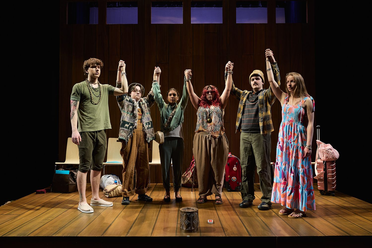 Six theater performers take a bow holding hands on a wooden stage during a curtain call performance.