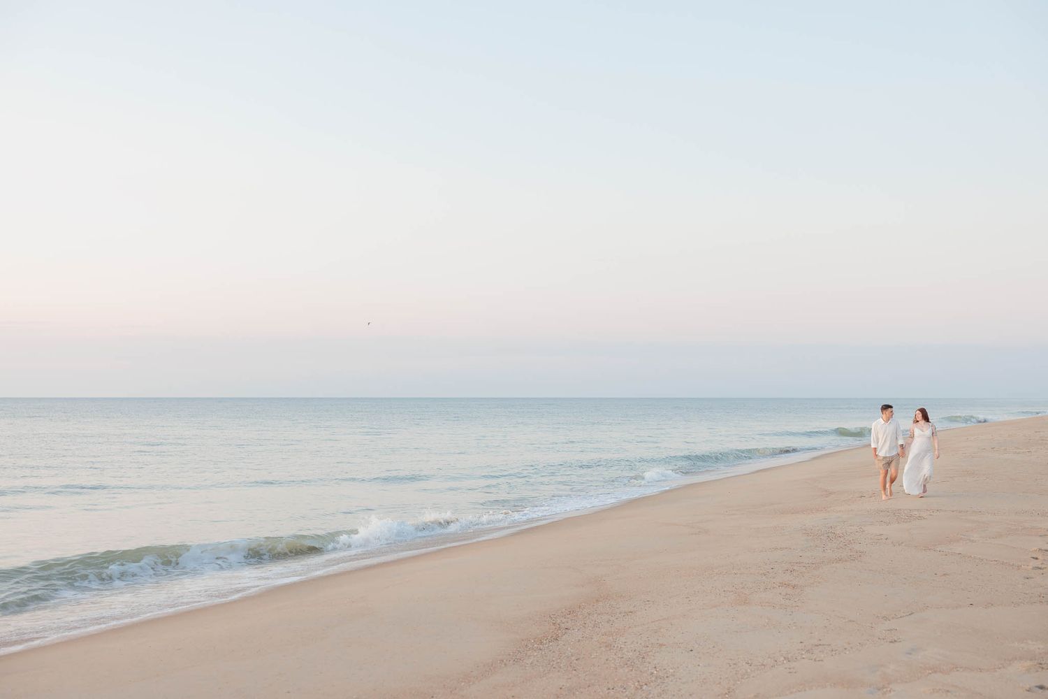 Serene beach landscape with white sand and ocean waves at sunset.