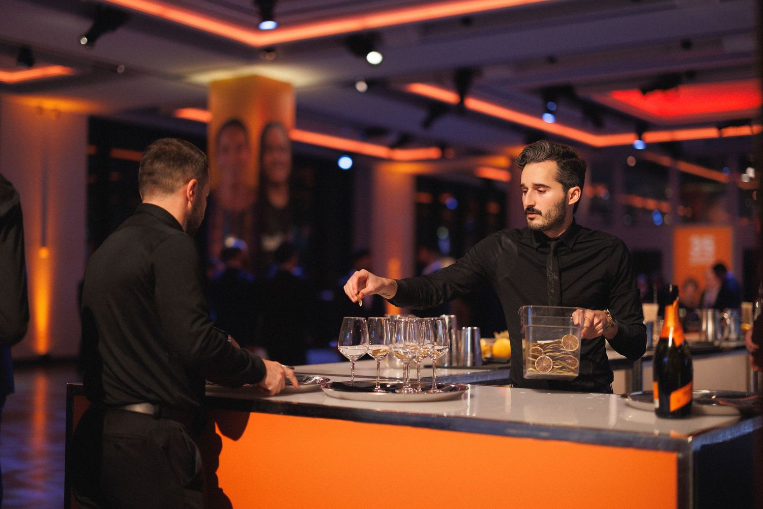 Bartender preparing cocktails at a dimly lit bar with orange and red ambient lighting.