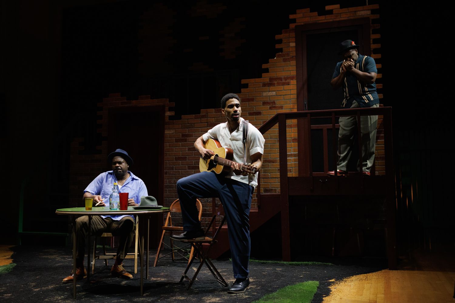 Musicians perform on a dimly lit stage with acoustic guitar and other instruments during a theatrical production.