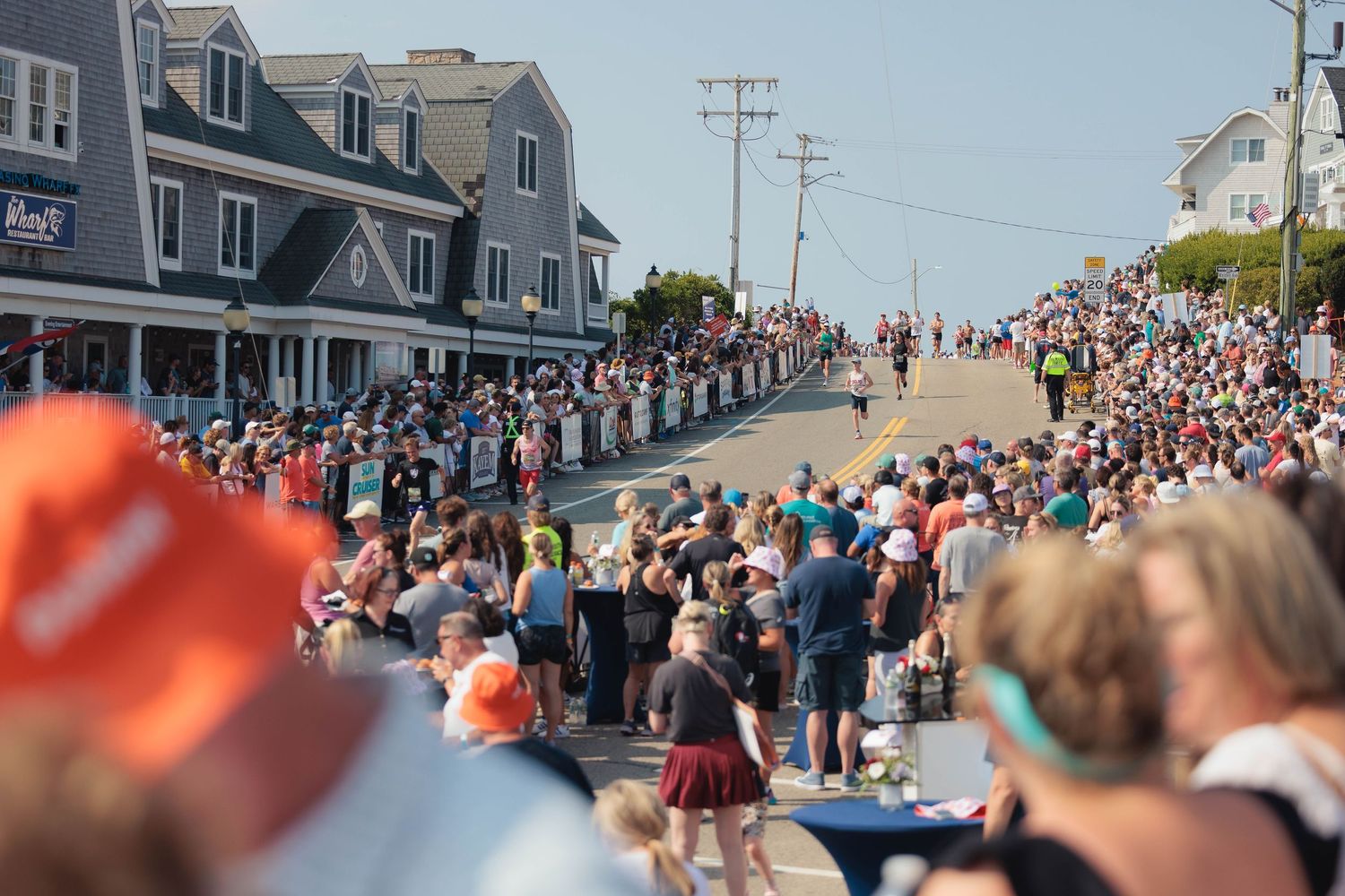 Large crowd of spectators line a steep hill at a street event in a coastal town.