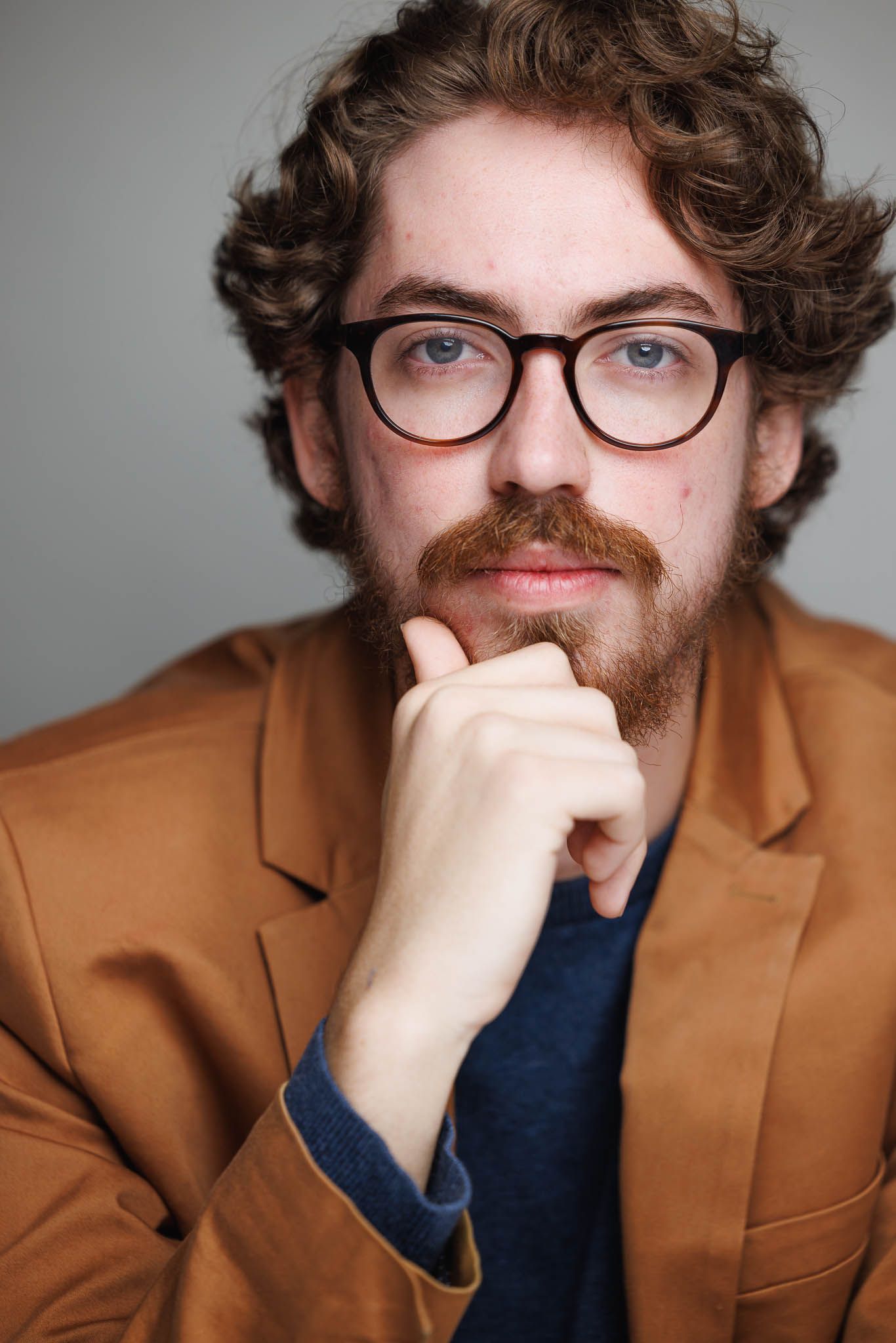 Professional headshots showing contemplative poses in brown blazer and blue shirt.
