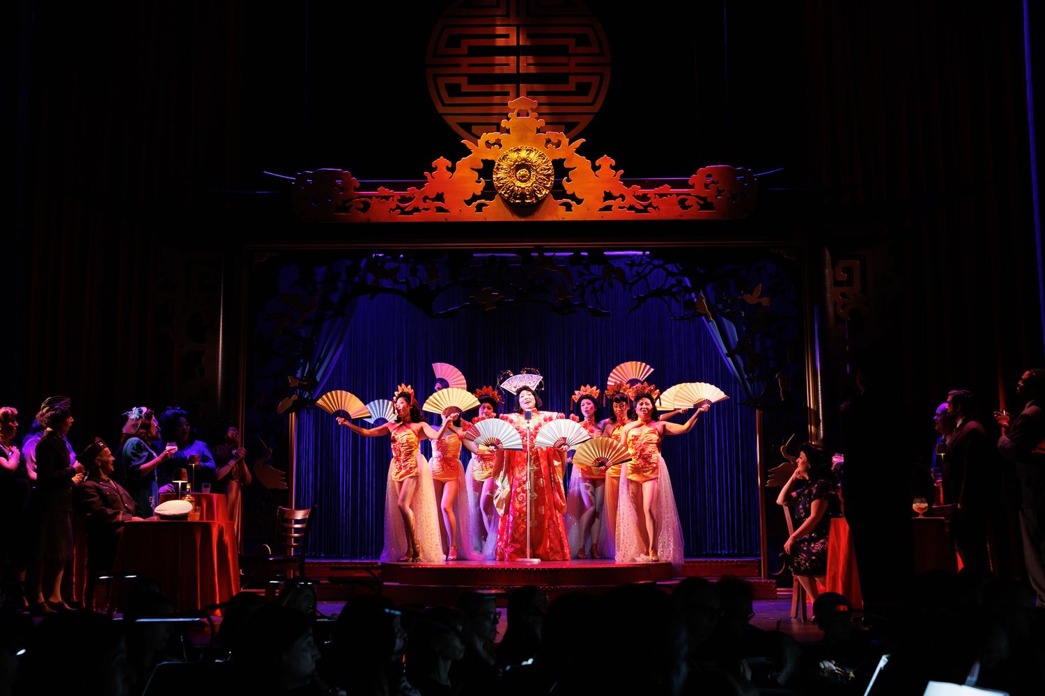 Colorful theatrical performance with performers in ornate costumes under dramatic lighting.