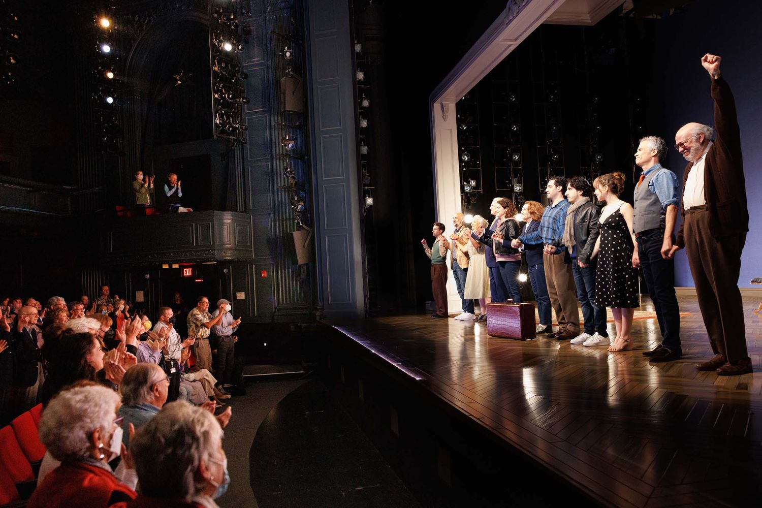 Performers take a bow on stage before an applauding audience in a packed theater.