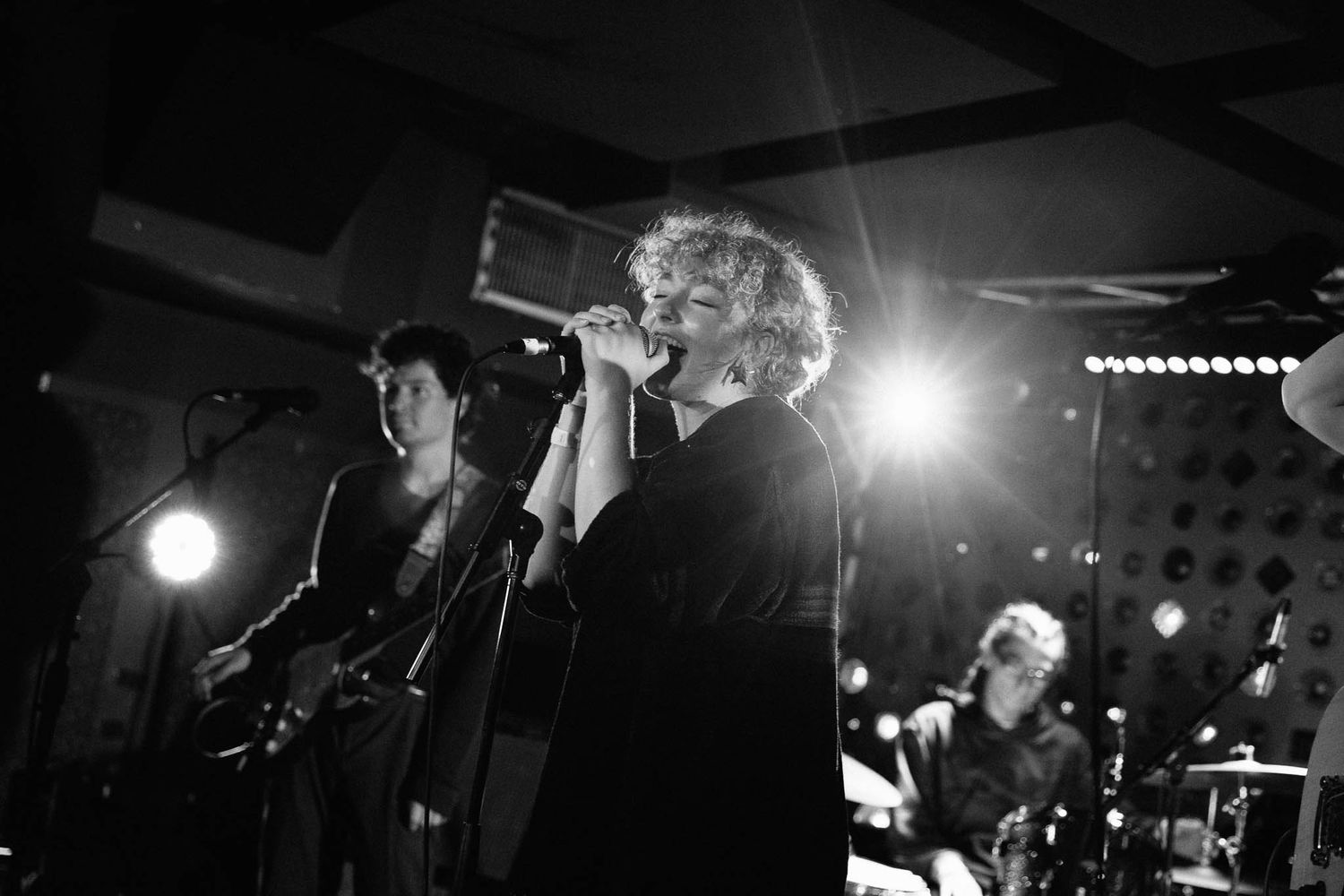 Black and white concert photo showing performers on stage with dramatic backlighting.