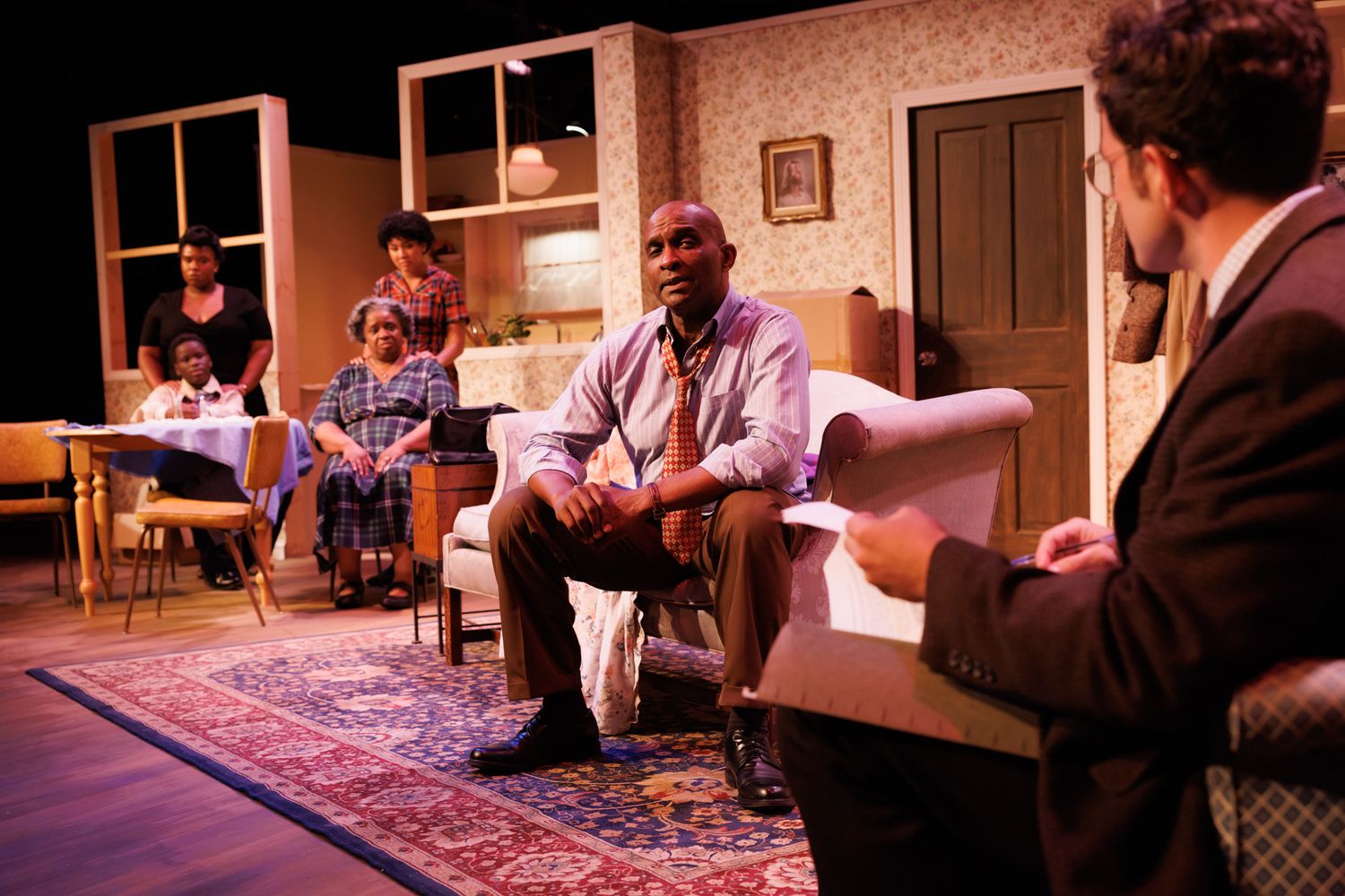 Theater scene showing dramatic indoor staging with warm lighting and period furniture.