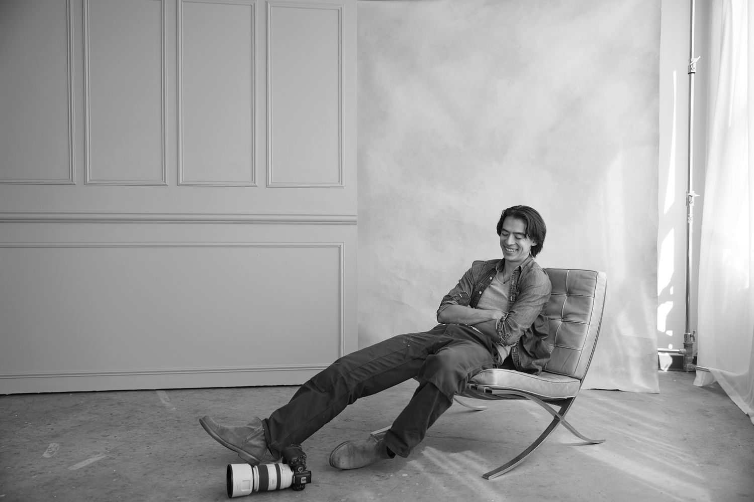 A person relaxes in a modern lounge chair against a white wall in a minimalist room, captured in black and white.