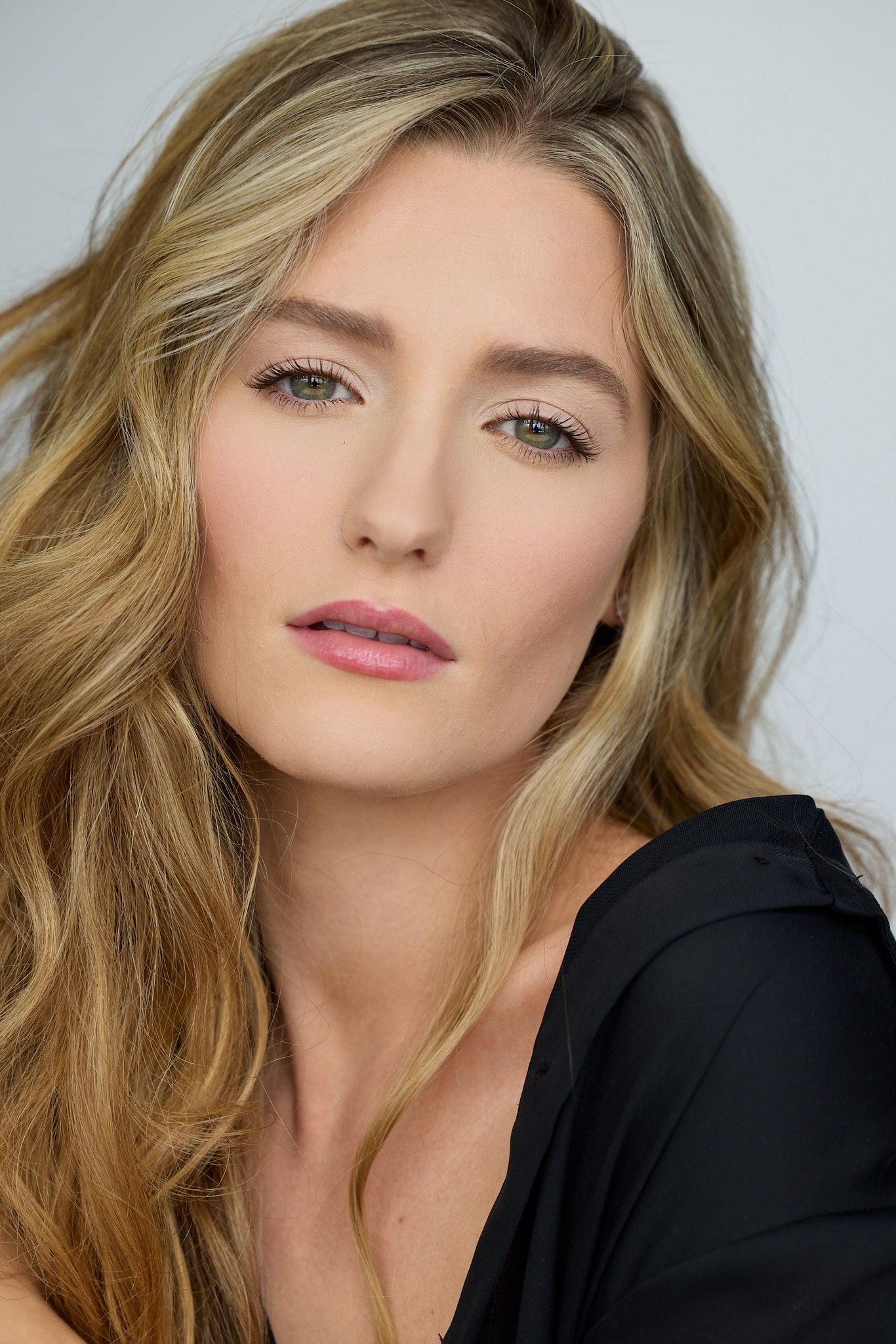 Close-up beauty portrait with blonde hair and natural makeup against light background.