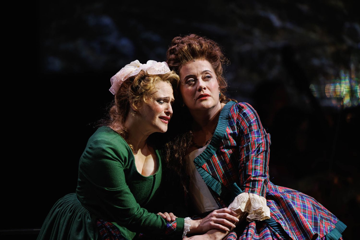 Theater actors performing an emotional scene together on a dimly lit stage.
