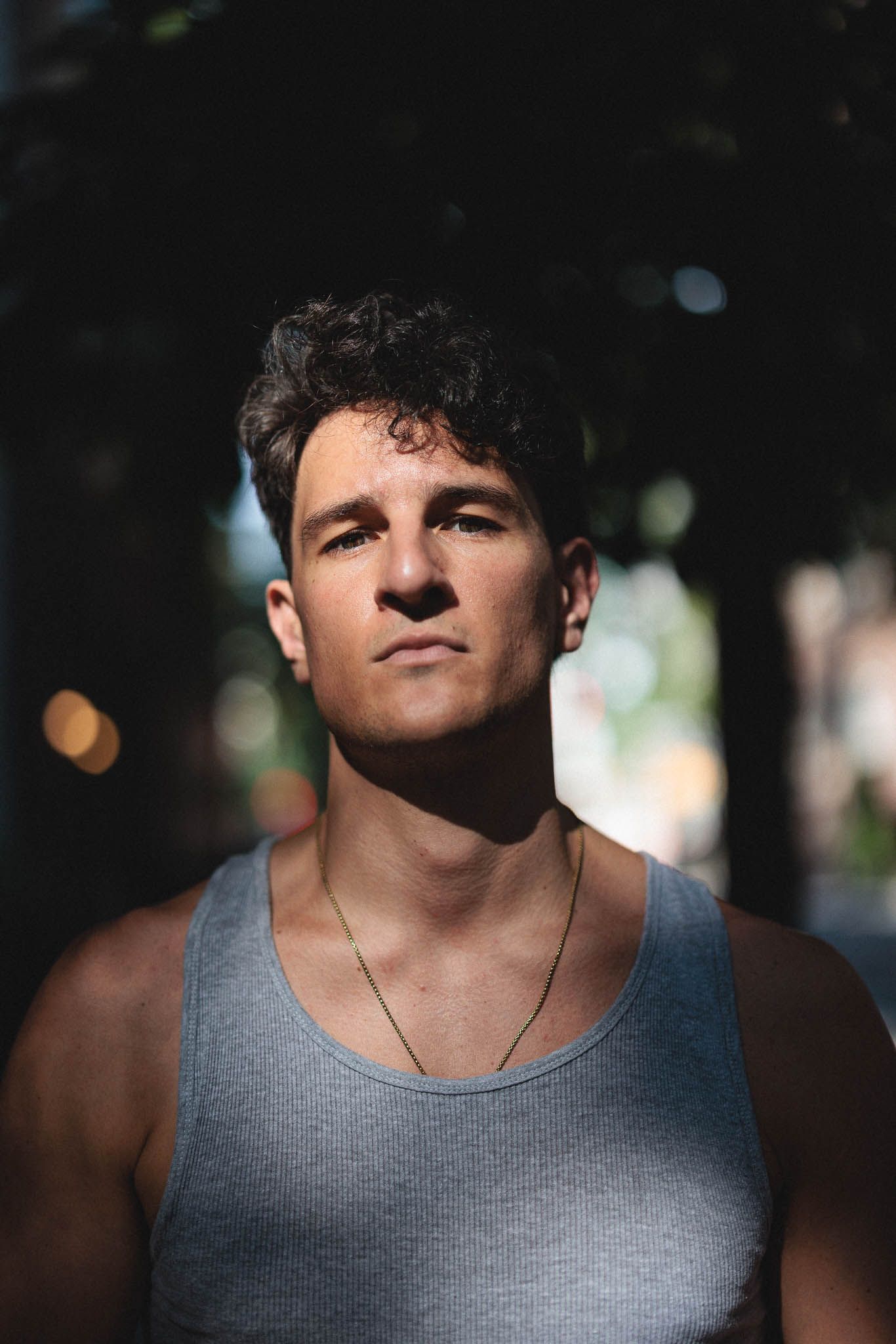 Portrait of a person in a grey tank top outdoors with natural lighting and bokeh background.