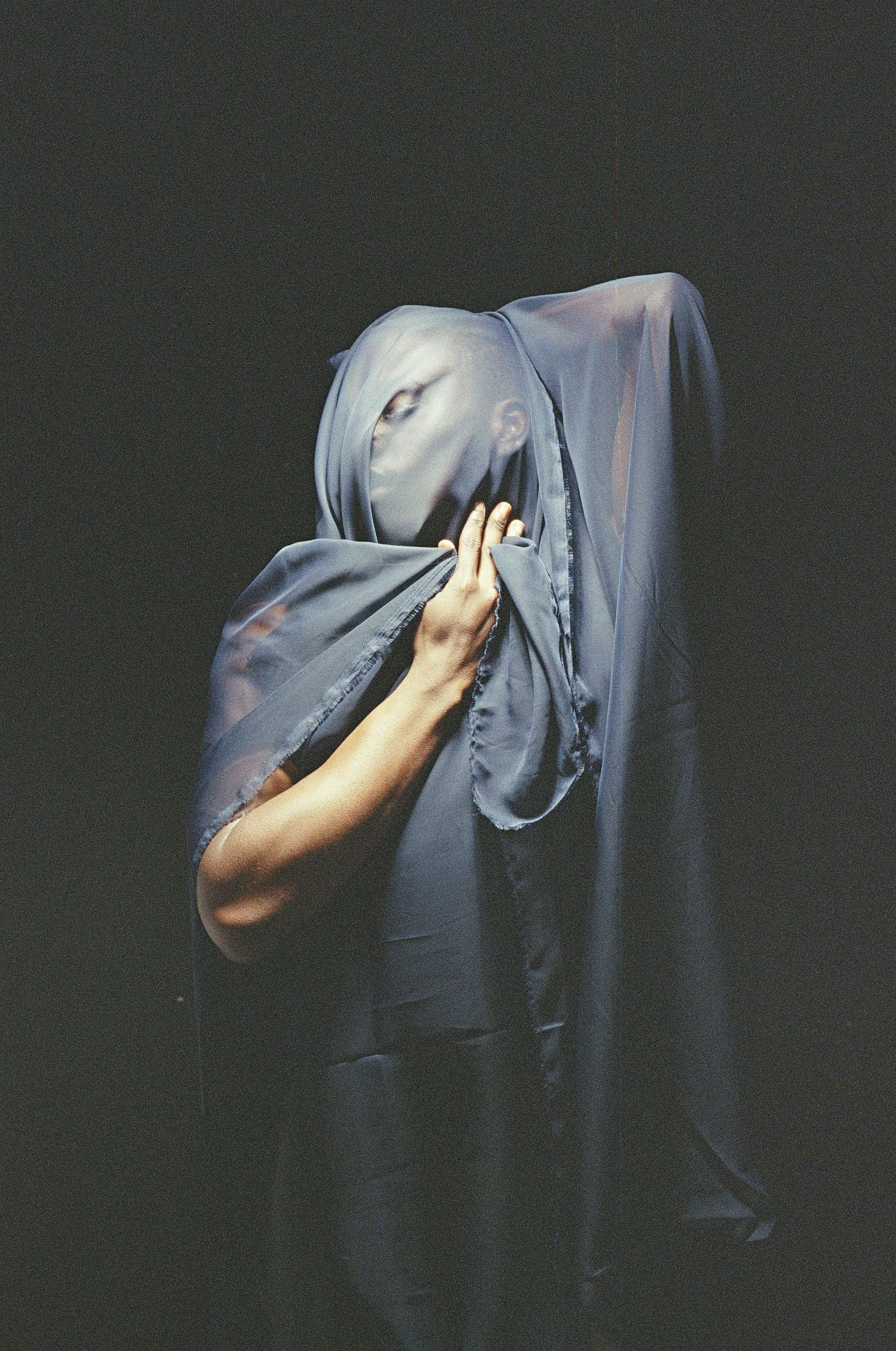 A series of artistic photographs showing a person struggling beneath grey fabric in a dark, moody setting.