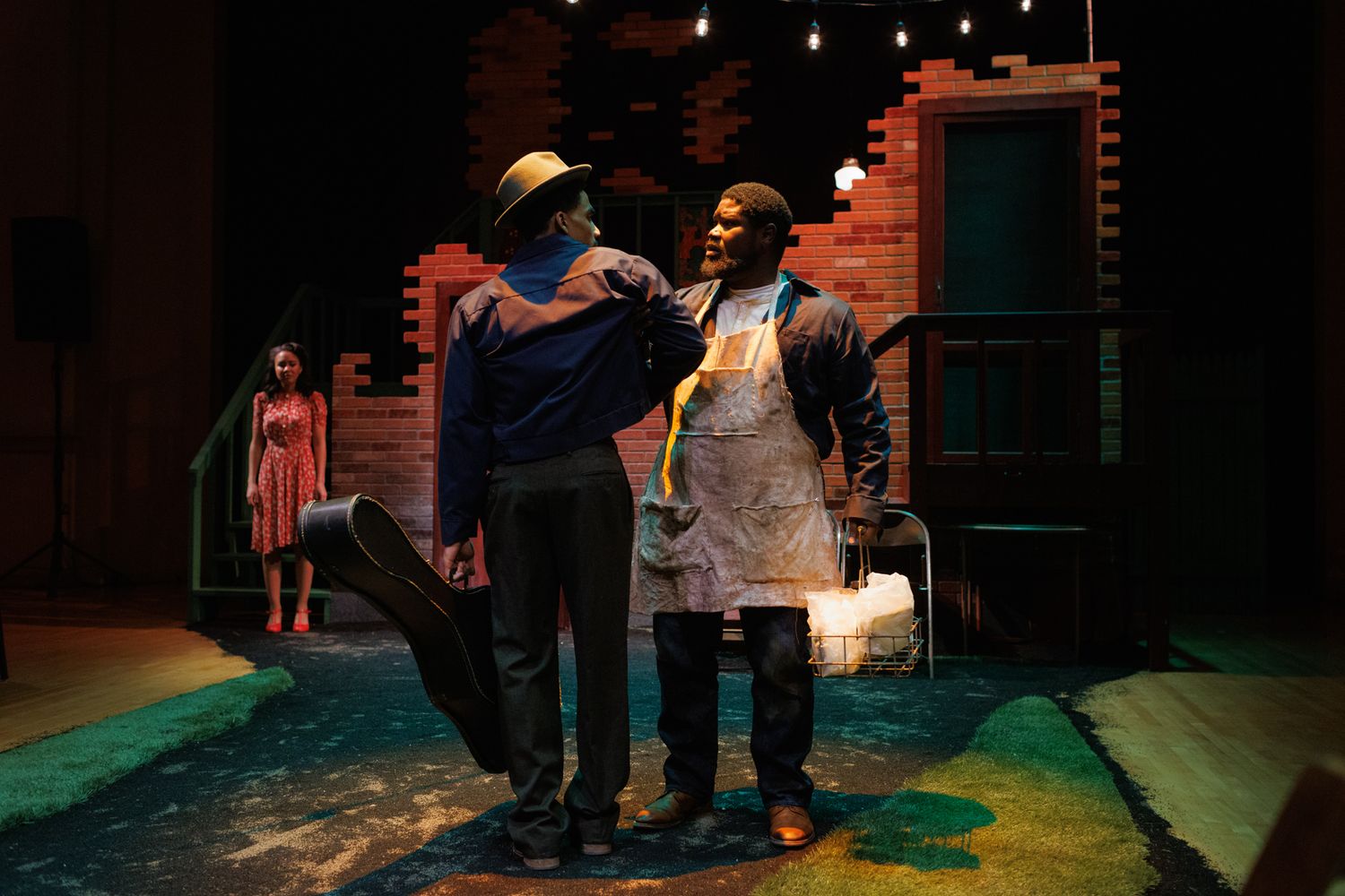 Two performers interact during scene on colorfully lit stage.