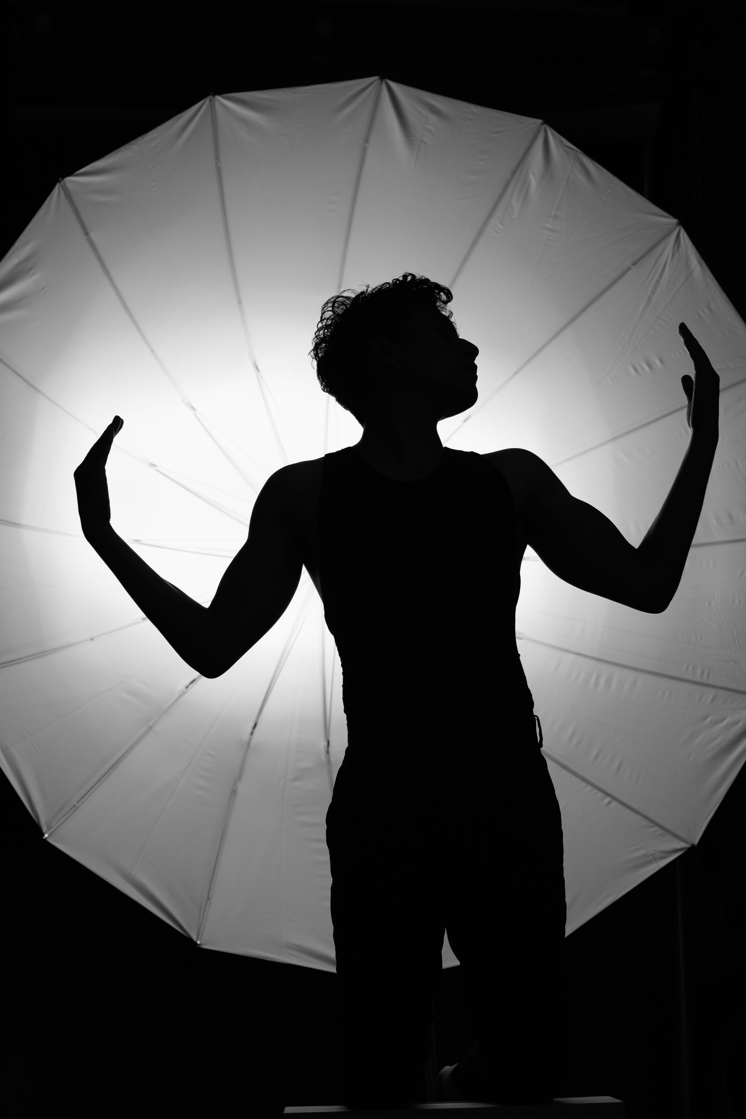 Dramatic silhouette of a performer against a backlit circular screen with outstretched arms in an artistic pose.