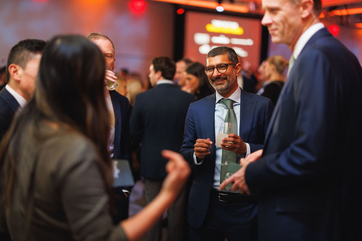 People mingling at an elegant evening event with ambient orange lighting and formal attire.