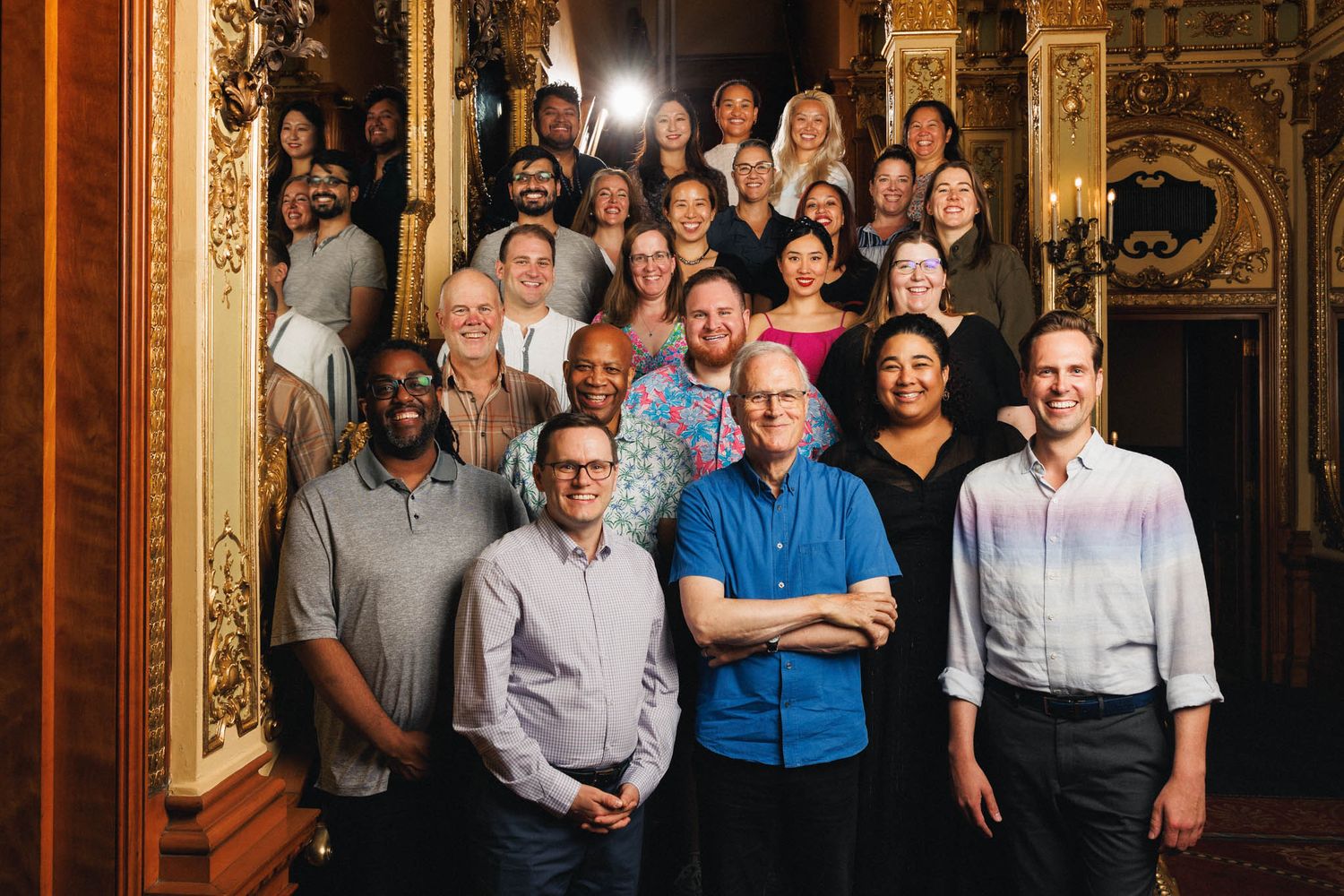 Large group photograph in an ornate vintage theater with gold decorative details.