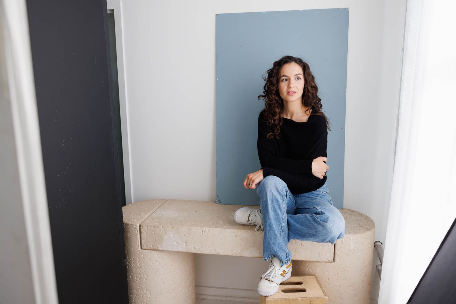 Casual studio portrait of person sitting on bench against blue backdrop.