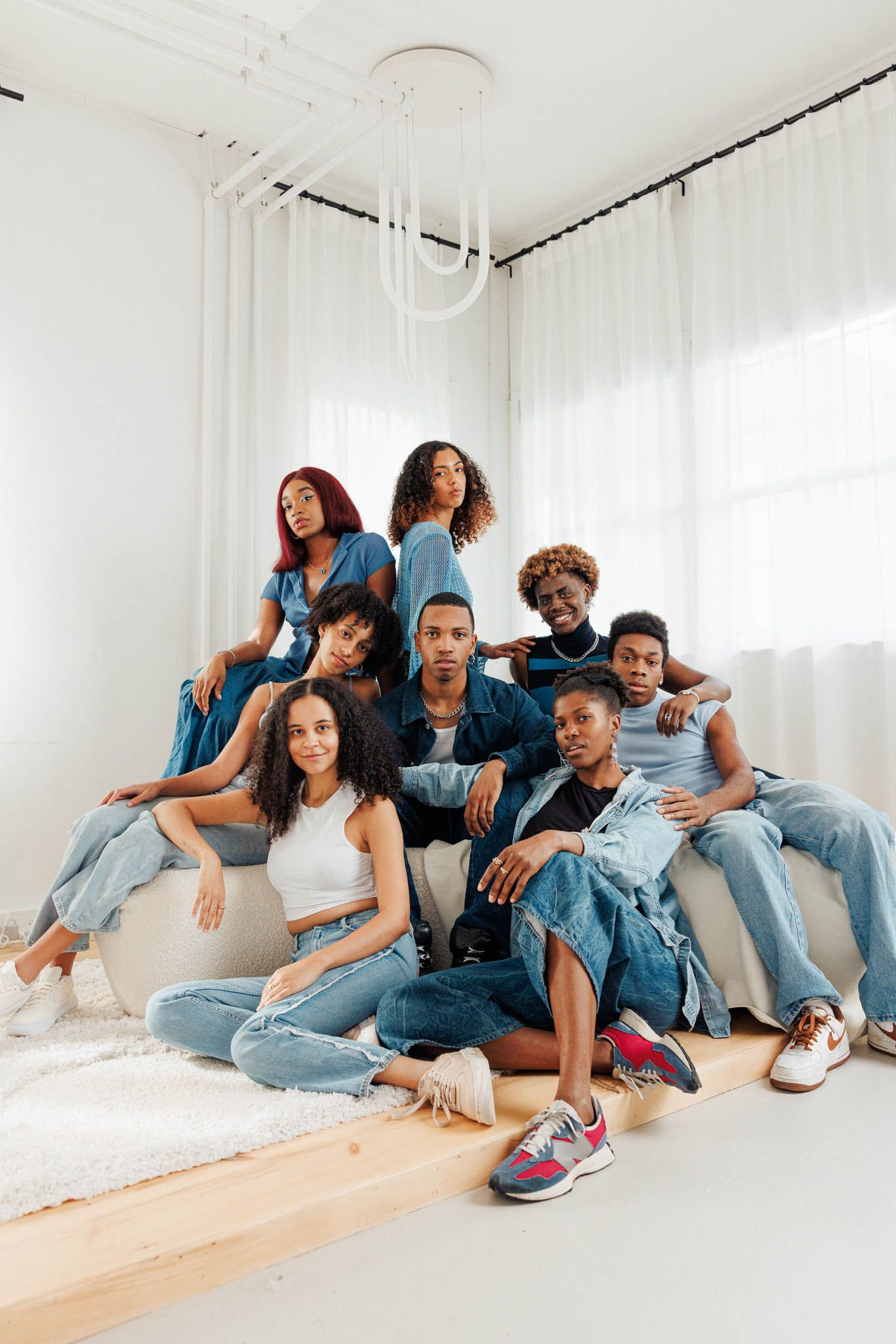Group portrait of actors in denim lounging casually against white studio walls.