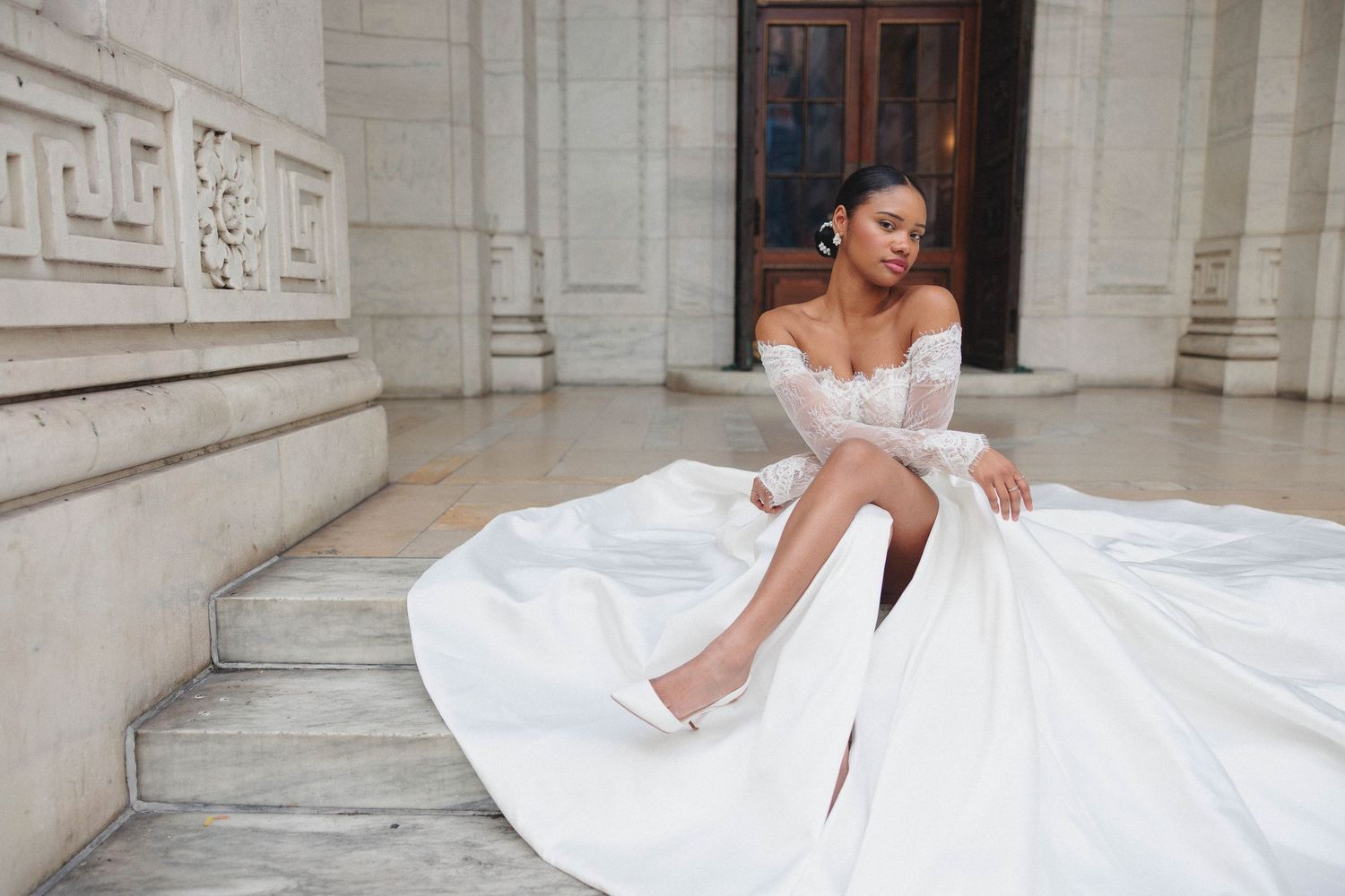 A bride in a voluminous white ball gown poses elegantly against a classic stone building exterior.