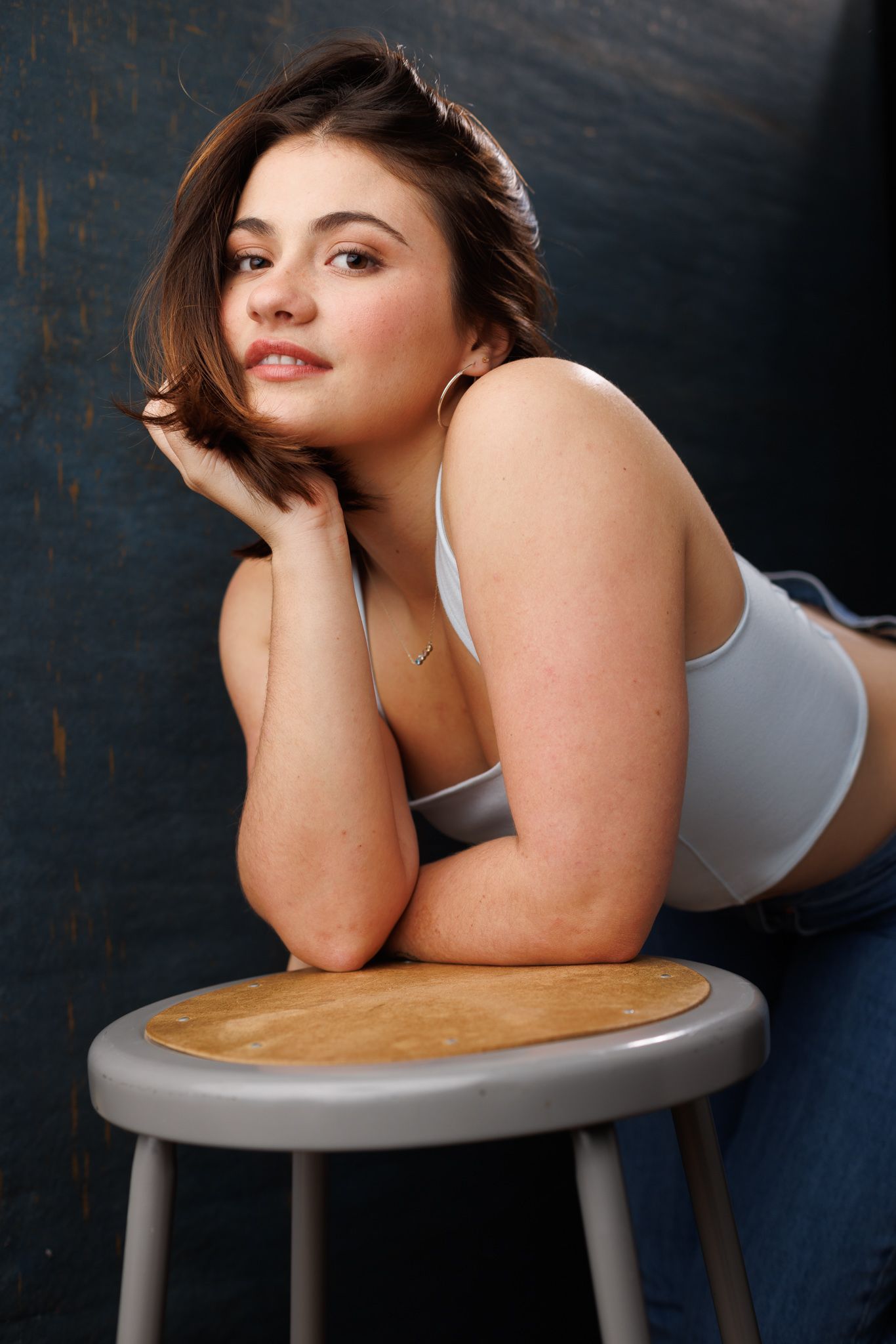 Portrait of a woman in activewear leaning on a stool against a dark background.